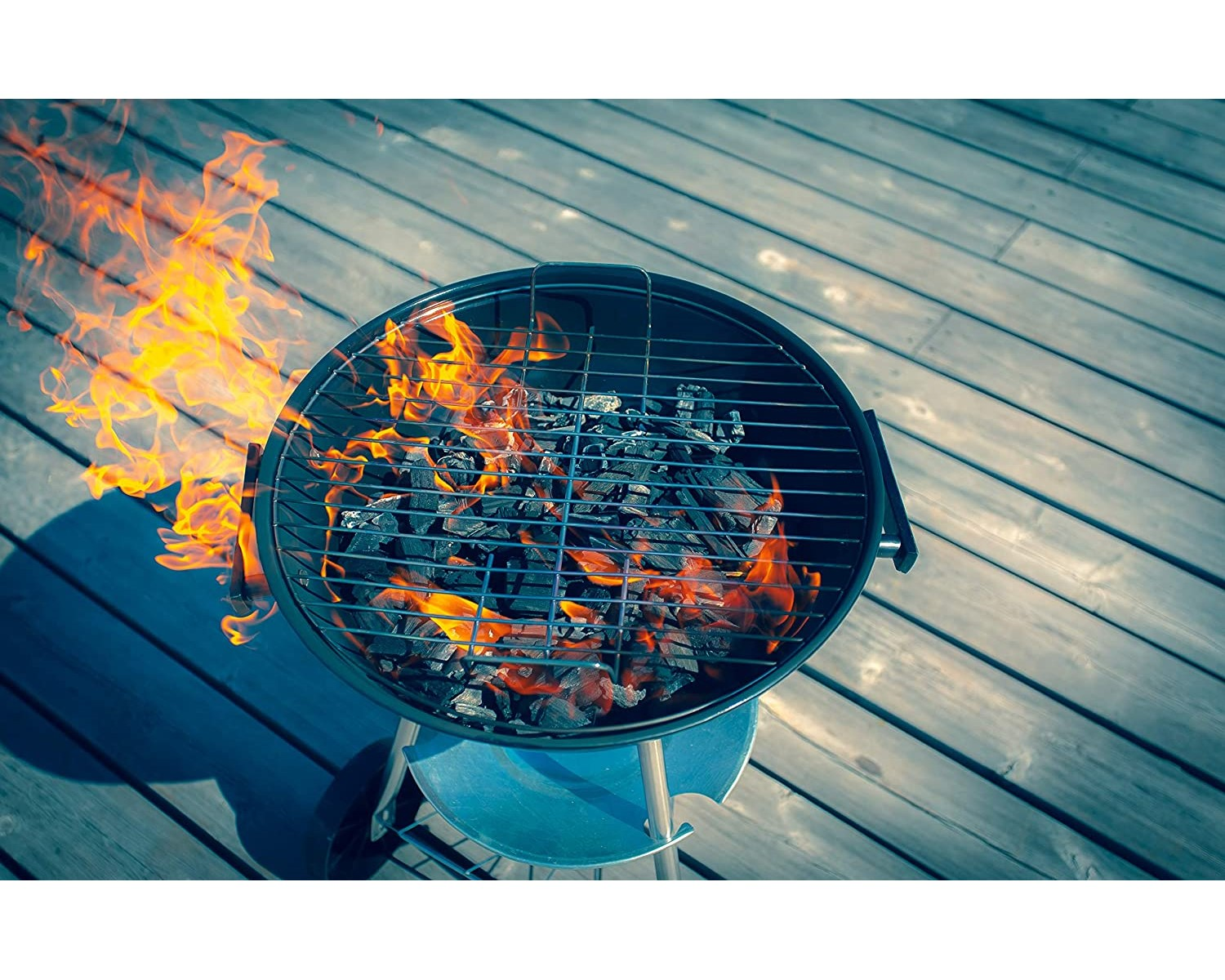 Ein runder Grill mit brennender Holzkohle und Flammen auf einem Holzdeck.