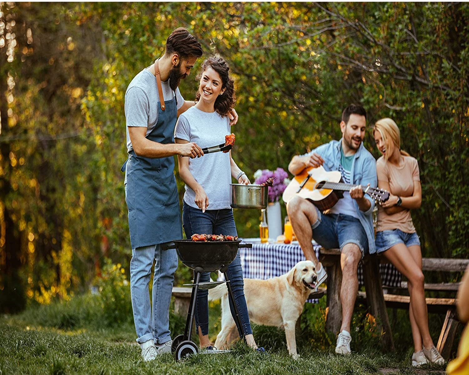 Leute grillen und spielen Gitarre draußen. Ein Hund ist dabei. Sonniger Tag.
