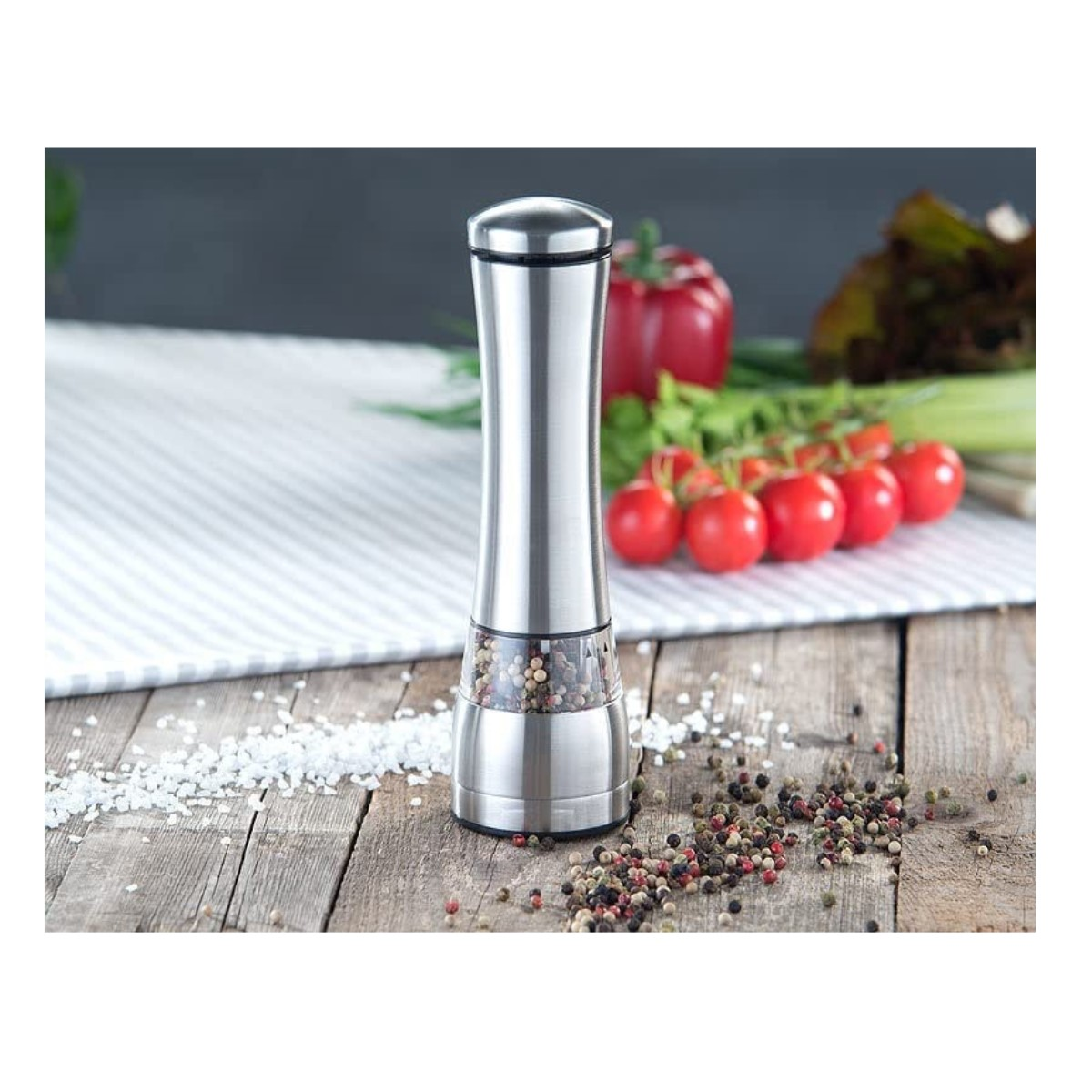 Pfeffermühle aus Edelstahl mit Pfefferkörnern und Tomaten auf einem Holztisch.
