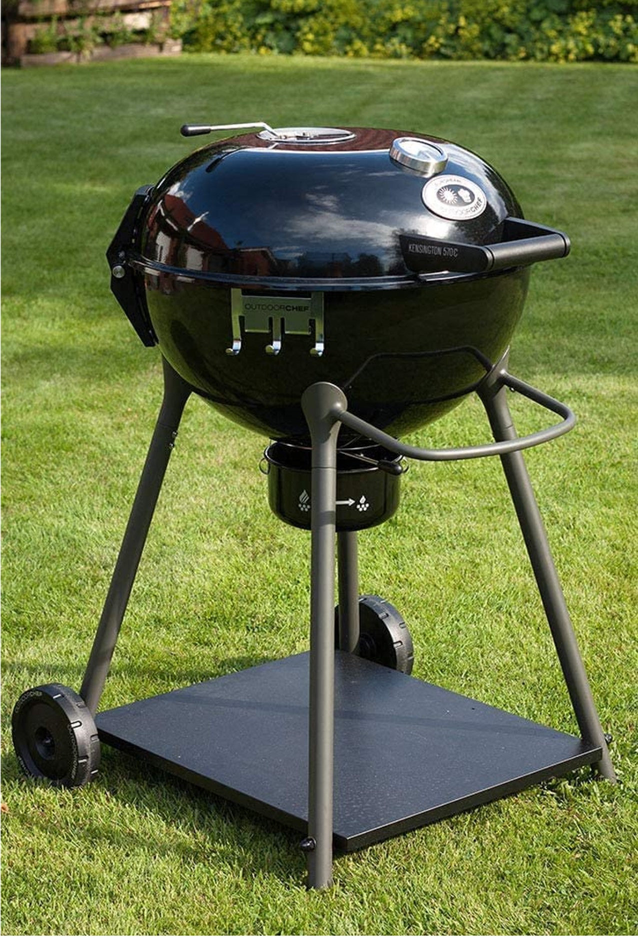 Schwarzer Outdoorchef-Grill auf grünem Gras. Er hat eine kugelförmige Form und steht auf einem rollbaren Ständer.
