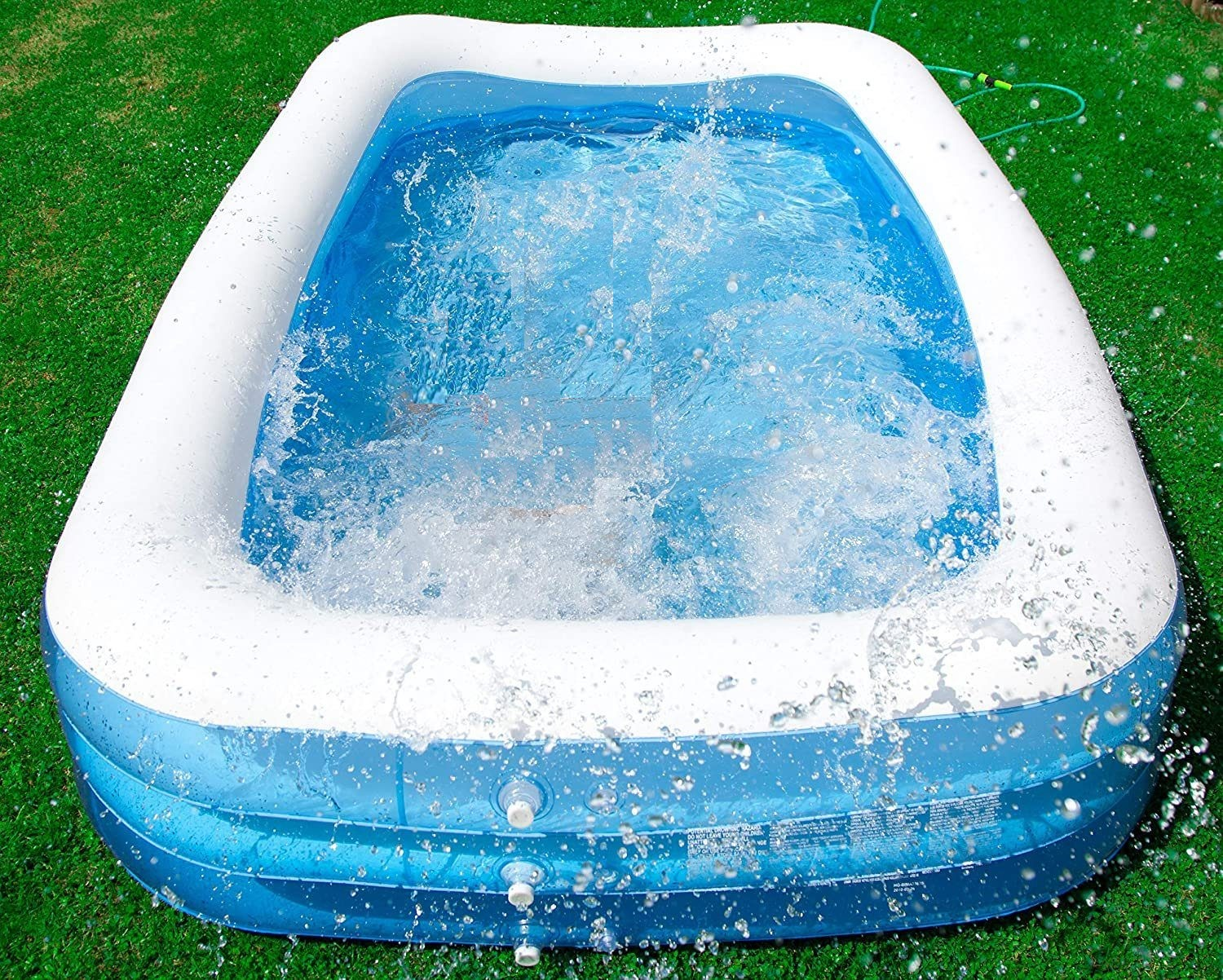 Viereckiger aufblasbarer Pool mit Wasser gefüllt, spritzend und überlaufend auf grünem Gras.