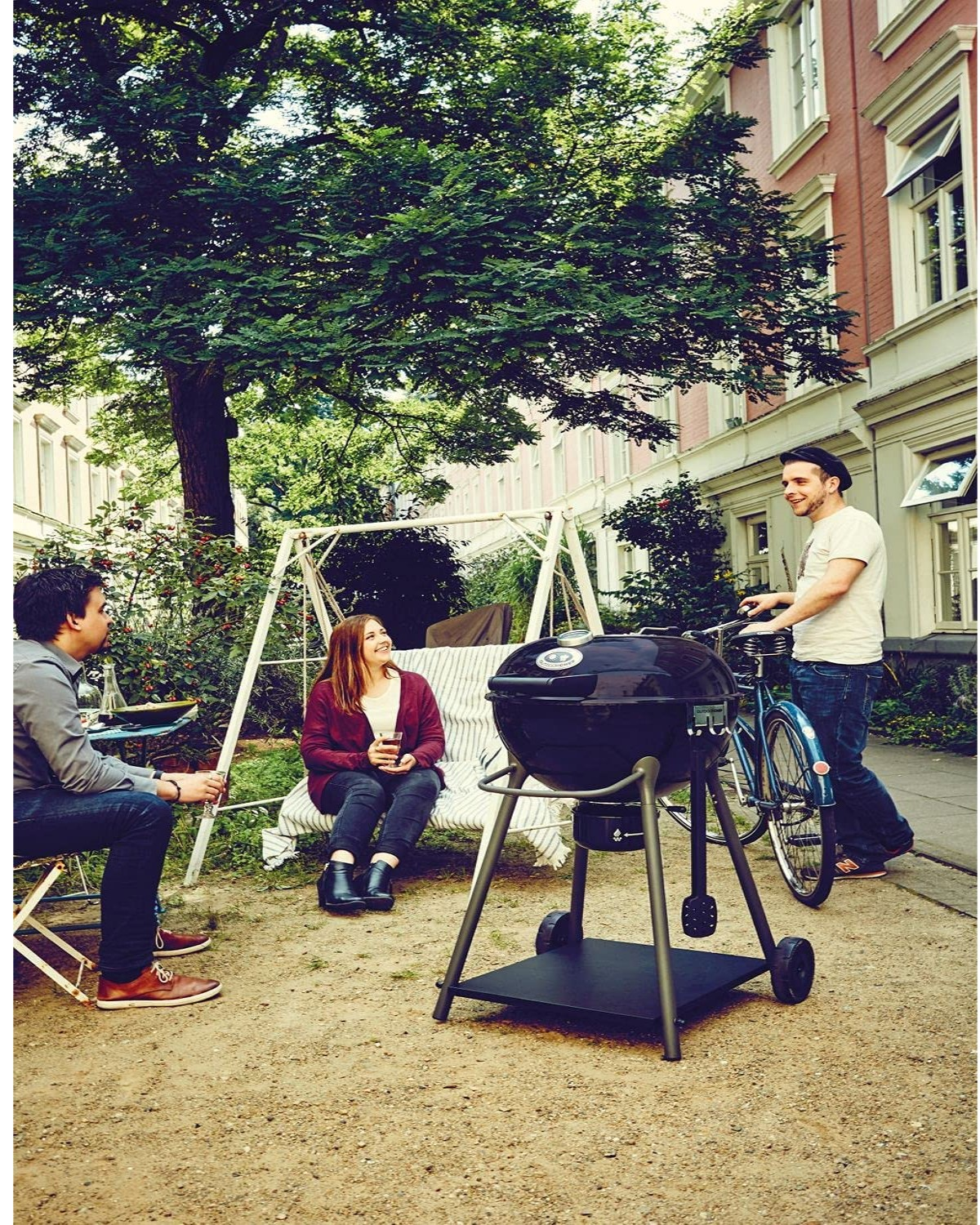 Leute grillen im Garten an einem Grill, mit Schaukel und großen Bäumen.