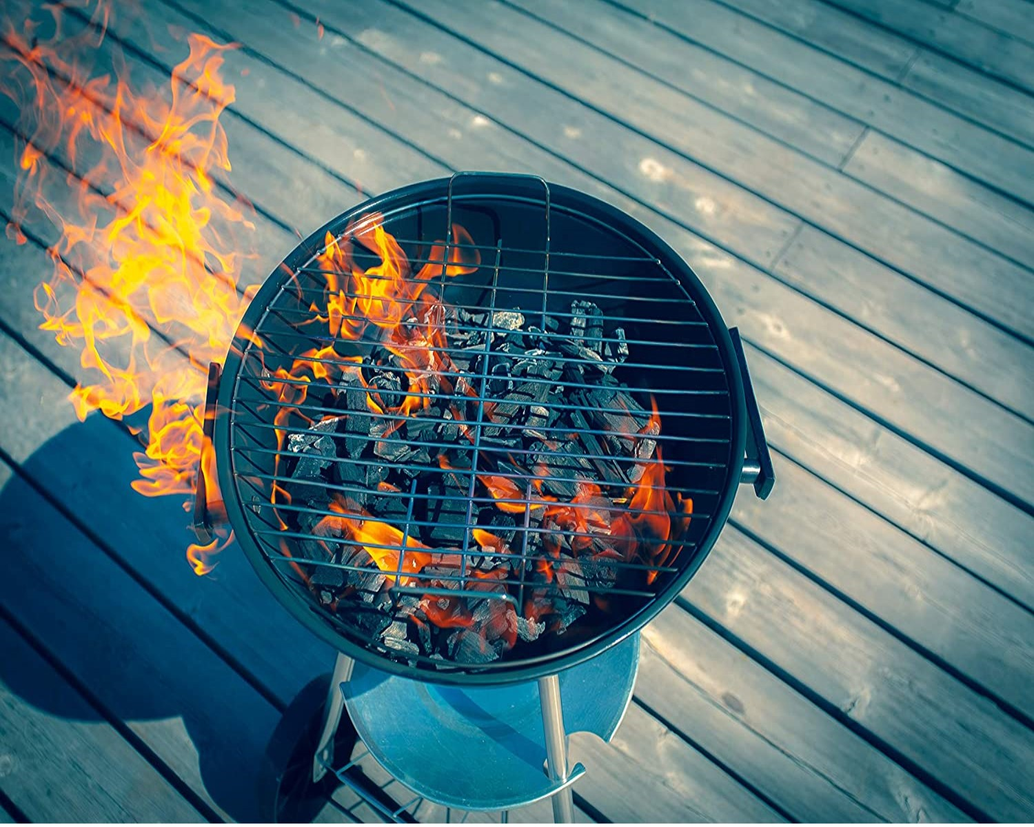 Ein runder schwarzer Grill mit brennender Holzkohle auf Holzterrassen.