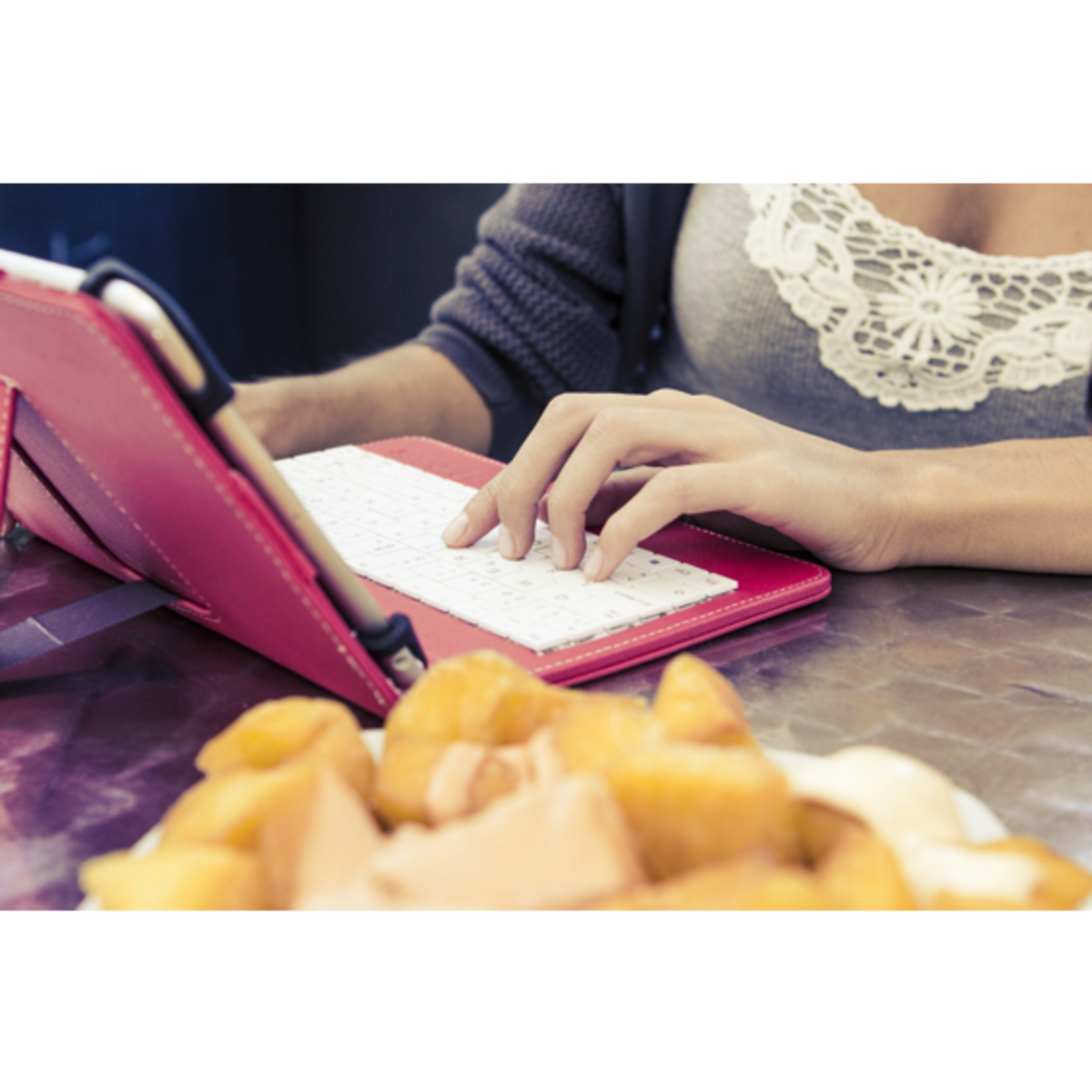Una persona usando una tableta con una funda de teclado, con comida en primer plano.