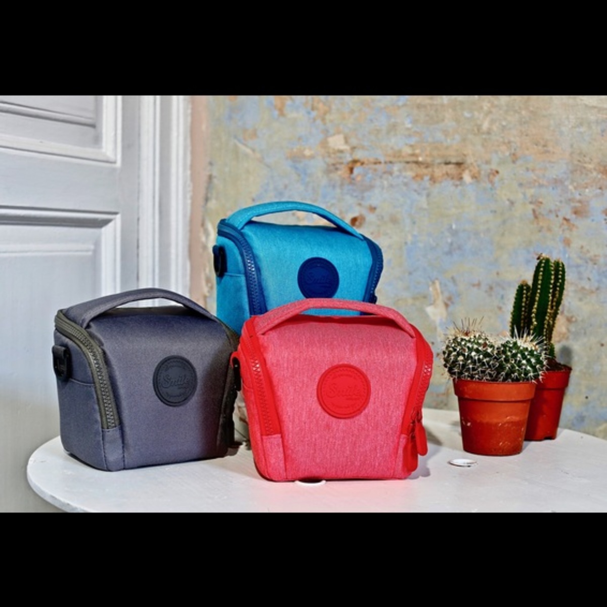 Tres bolsas de cámara coloridas en una mesa blanca con cactus detrás.