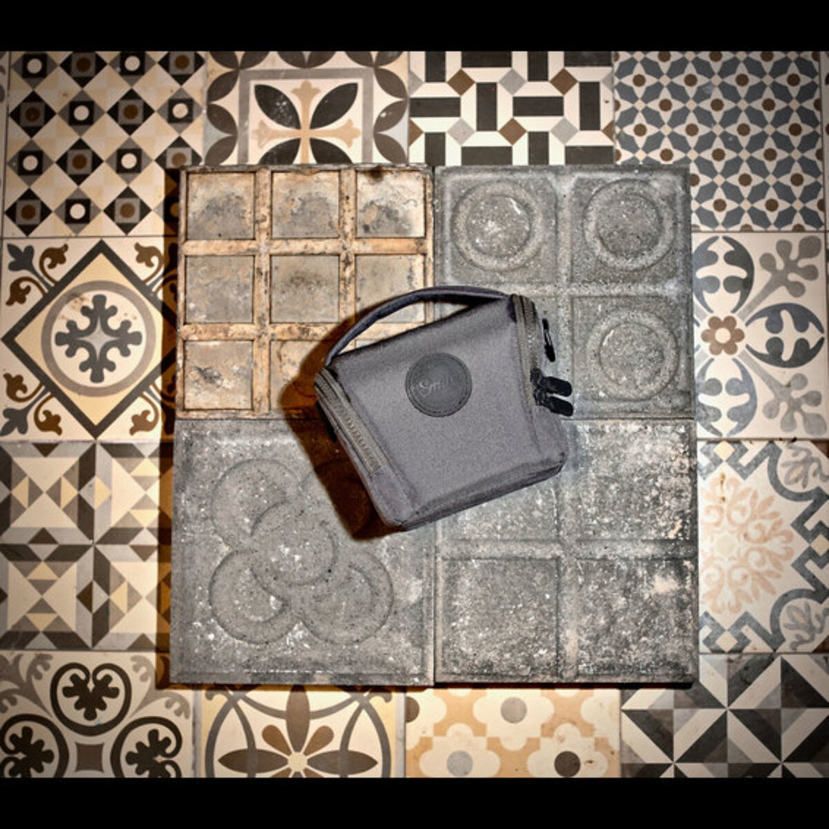 Una bolsa de cámara gris sobre un suelo de baldosas estampadas. Las baldosas tienen diseños geométricos y florales.