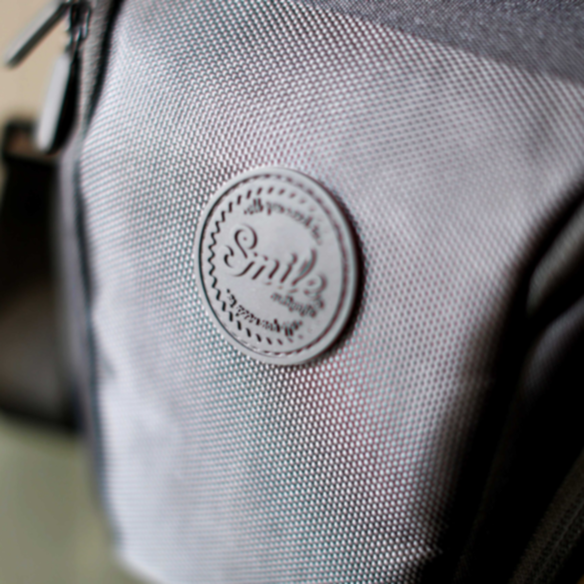 Primer plano de una bolsa gris con un parche redondo que dice "Smile".