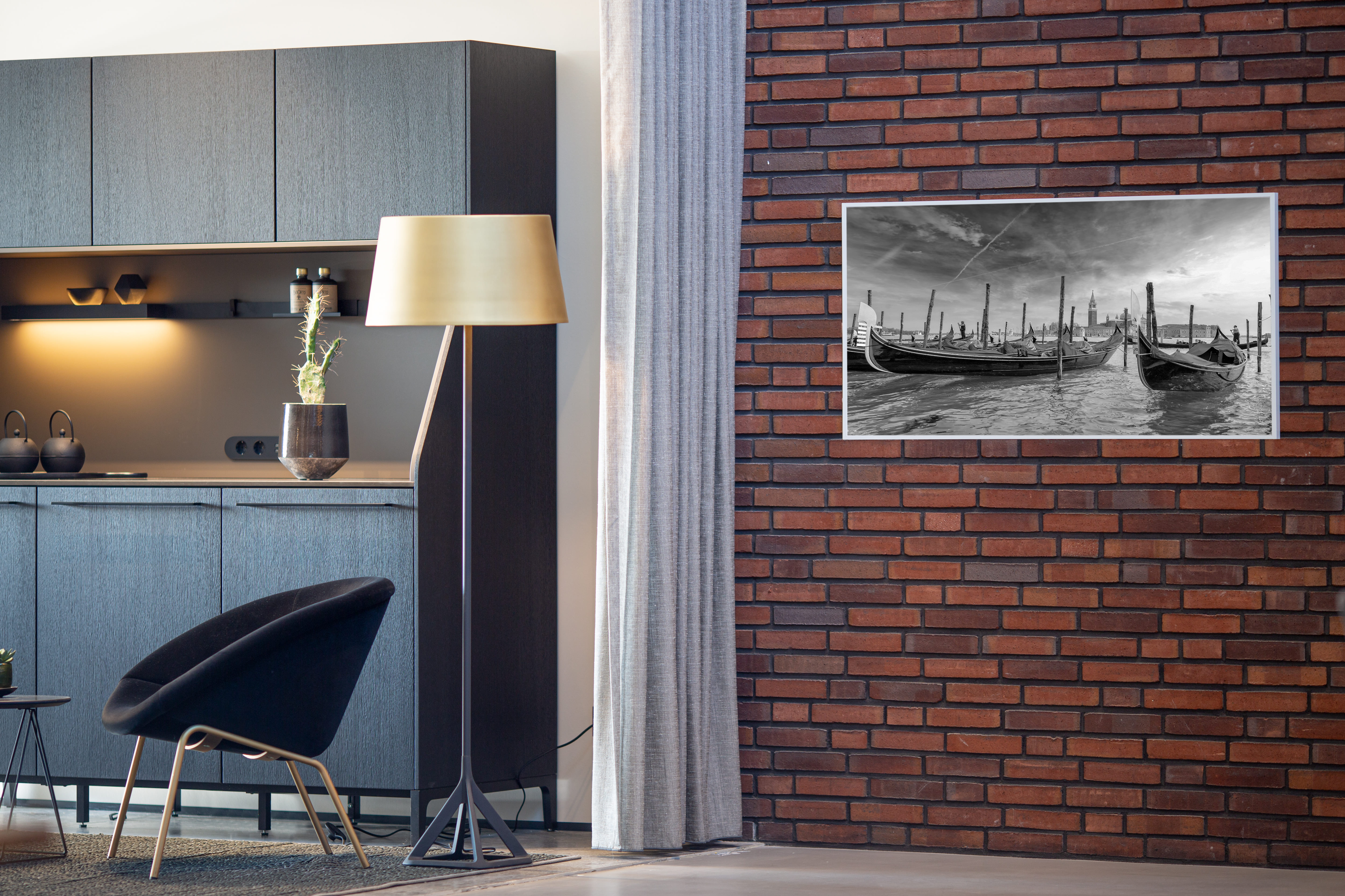 Ein modernes Interieur mit Backsteinmauer, schwarzem Stuhl, Stehleuchte und einem Bild einer Kanalszene.
