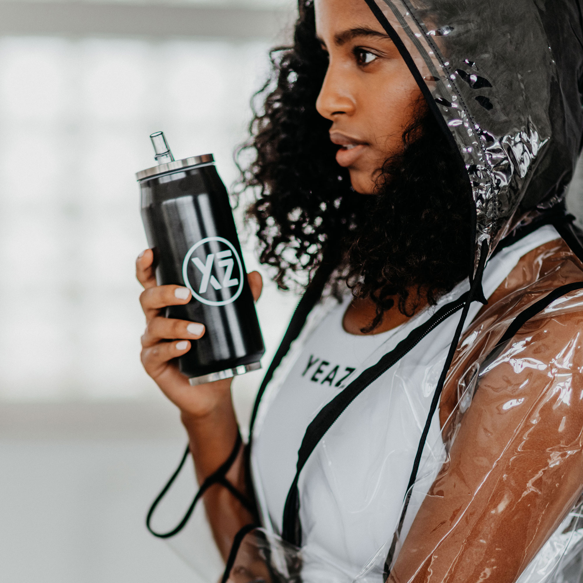 Mujer con una botella negra en forma de lata, usando una chaqueta impermeable transparente.