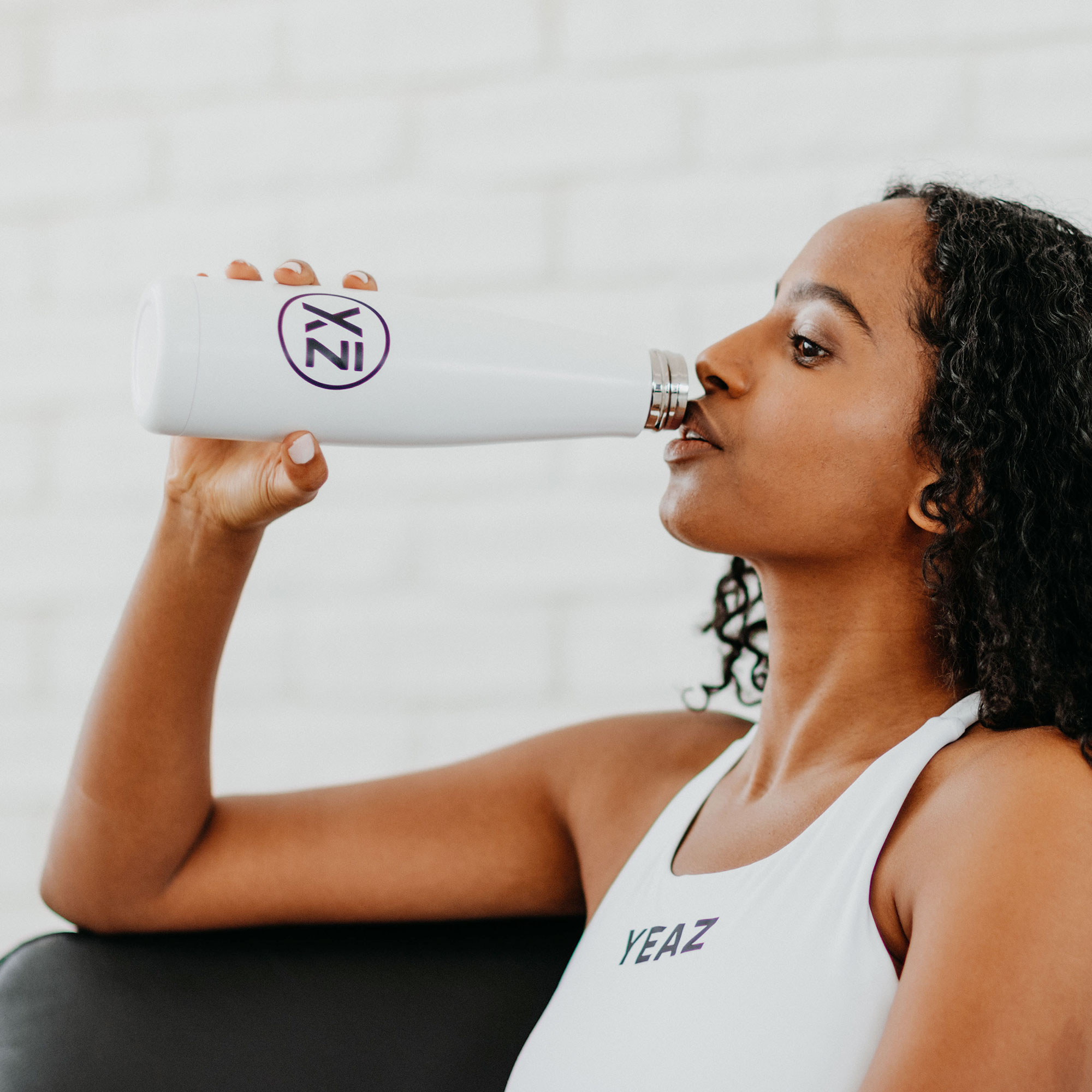 Mujer bebiendo de una botella de agua blanca con logo.