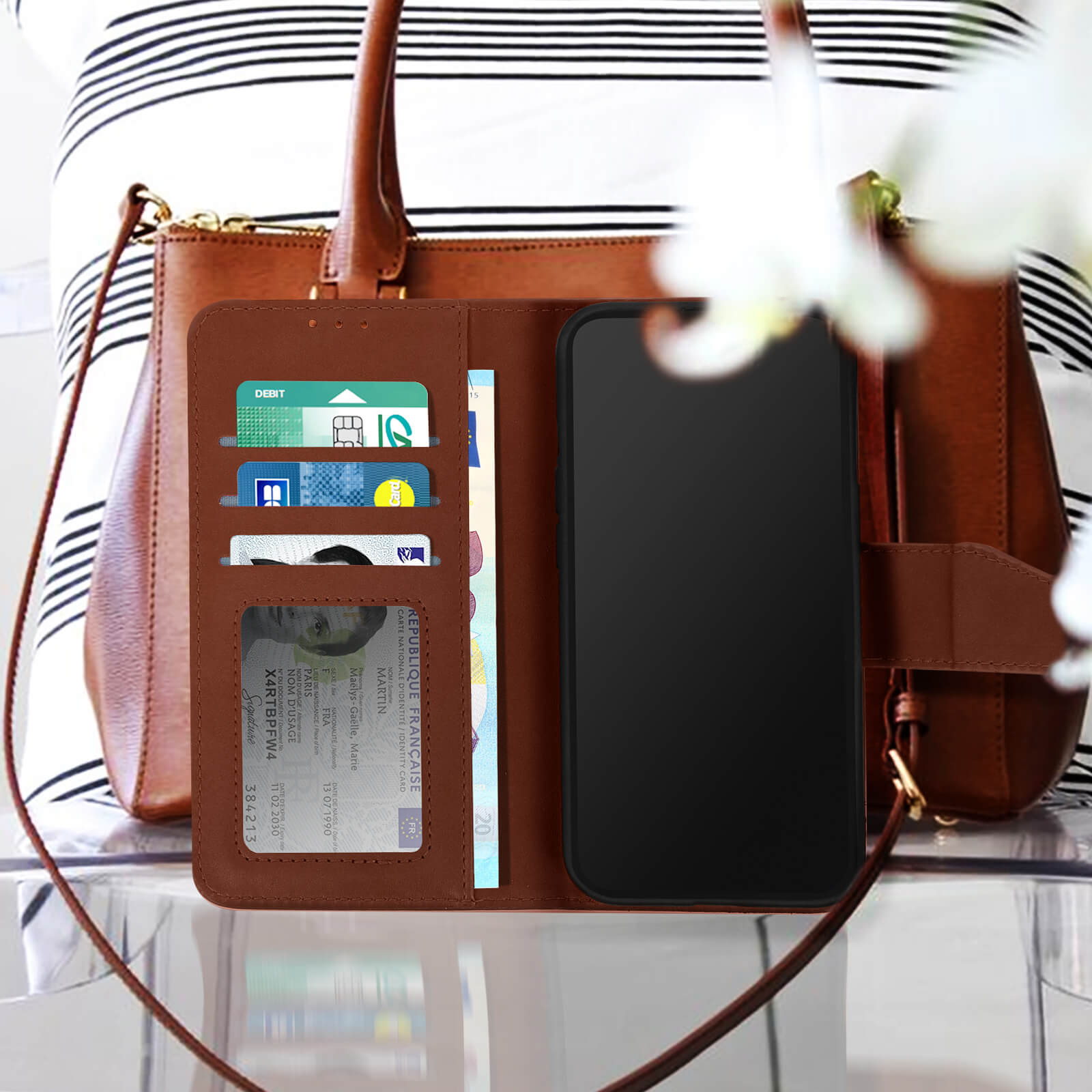 Smartphone in custodia a portafoglio marrone, aperto, con carte e ID visibili, vicino a una borsa.