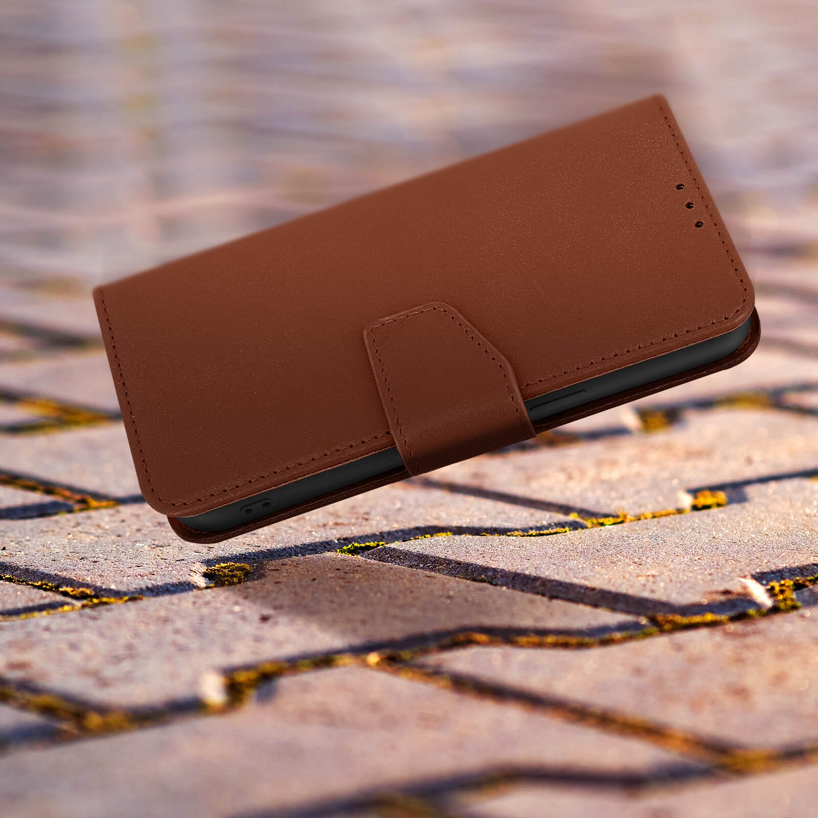 Bruine leren telefoonhoes met een druksluiting, liggend op een gestructureerd oppervlak.