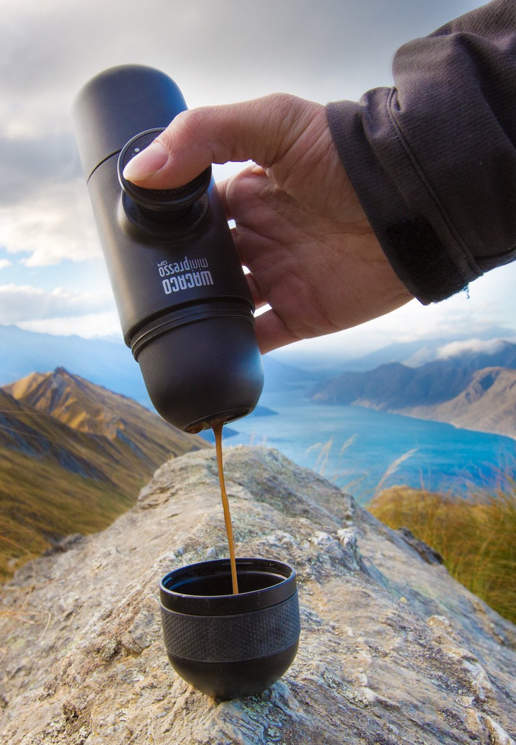 Person gießt Kaffee aus einem tragbaren Espressokocher in eine Tasse im Freien.