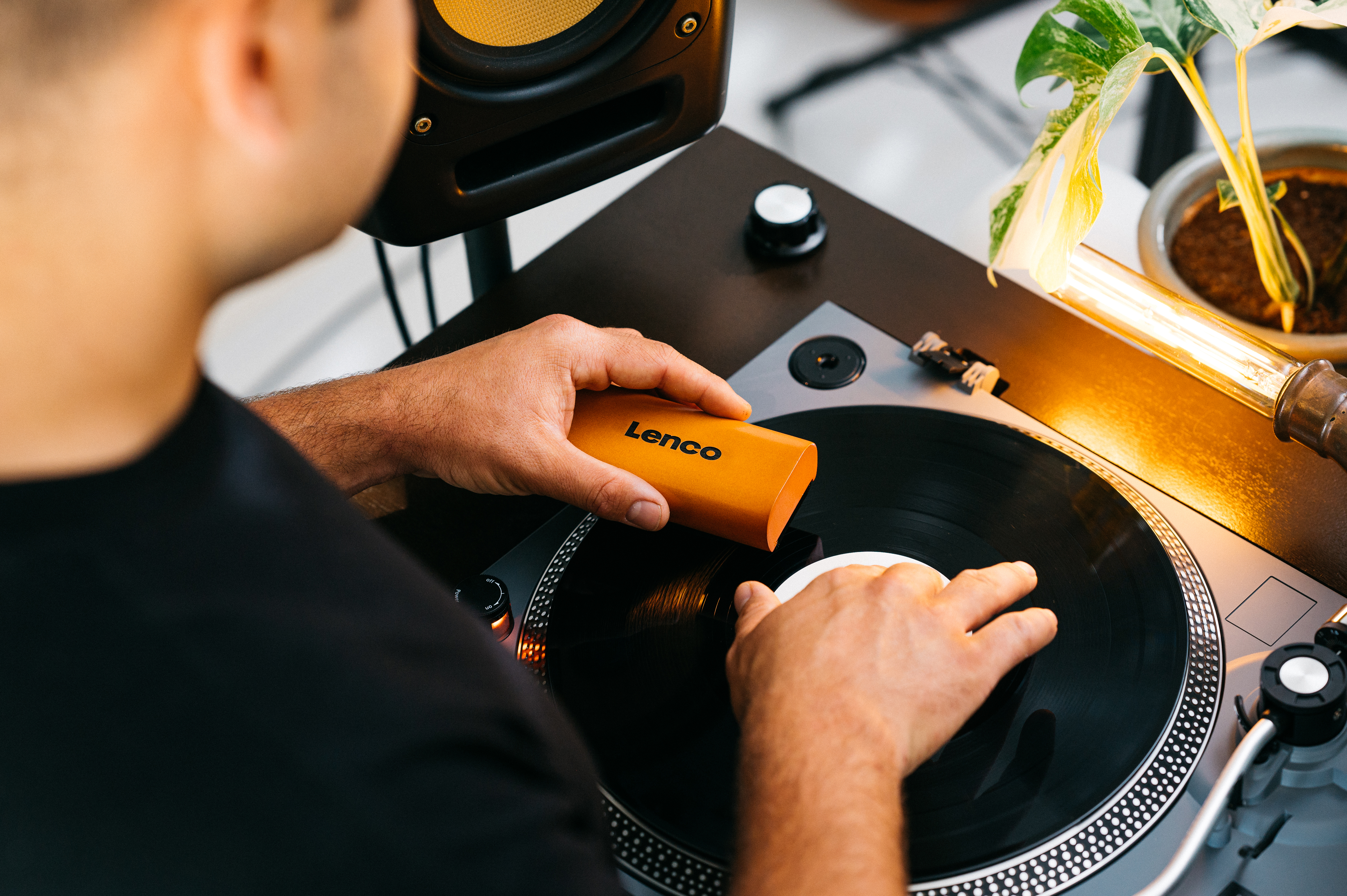 Persona limpiando un disco de vinilo en un tocadiscos con un cepillo Lenco naranja.