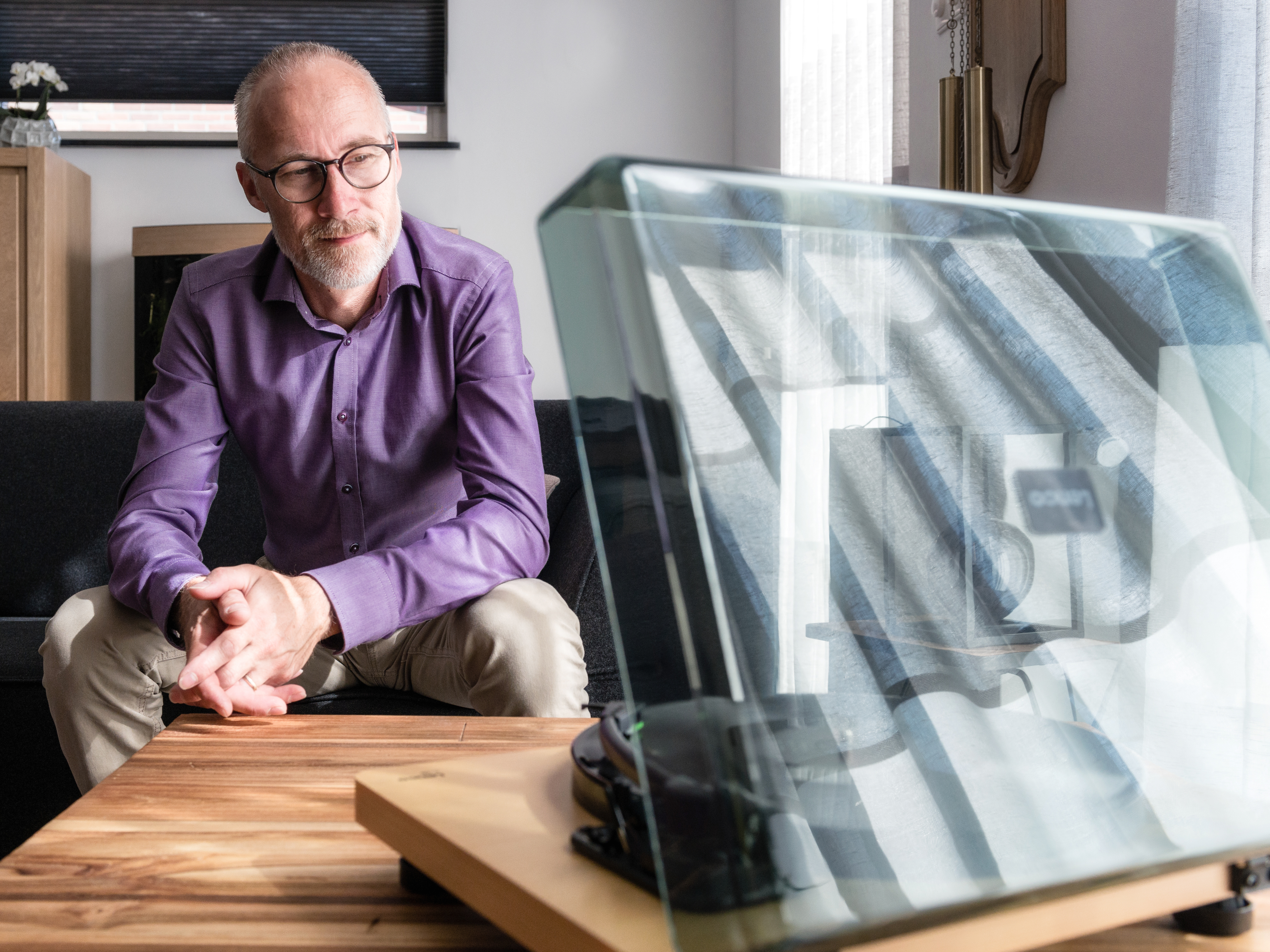 Mężczyzna siedzi, patrząc na gramofon. Szklana osłona z przodu.