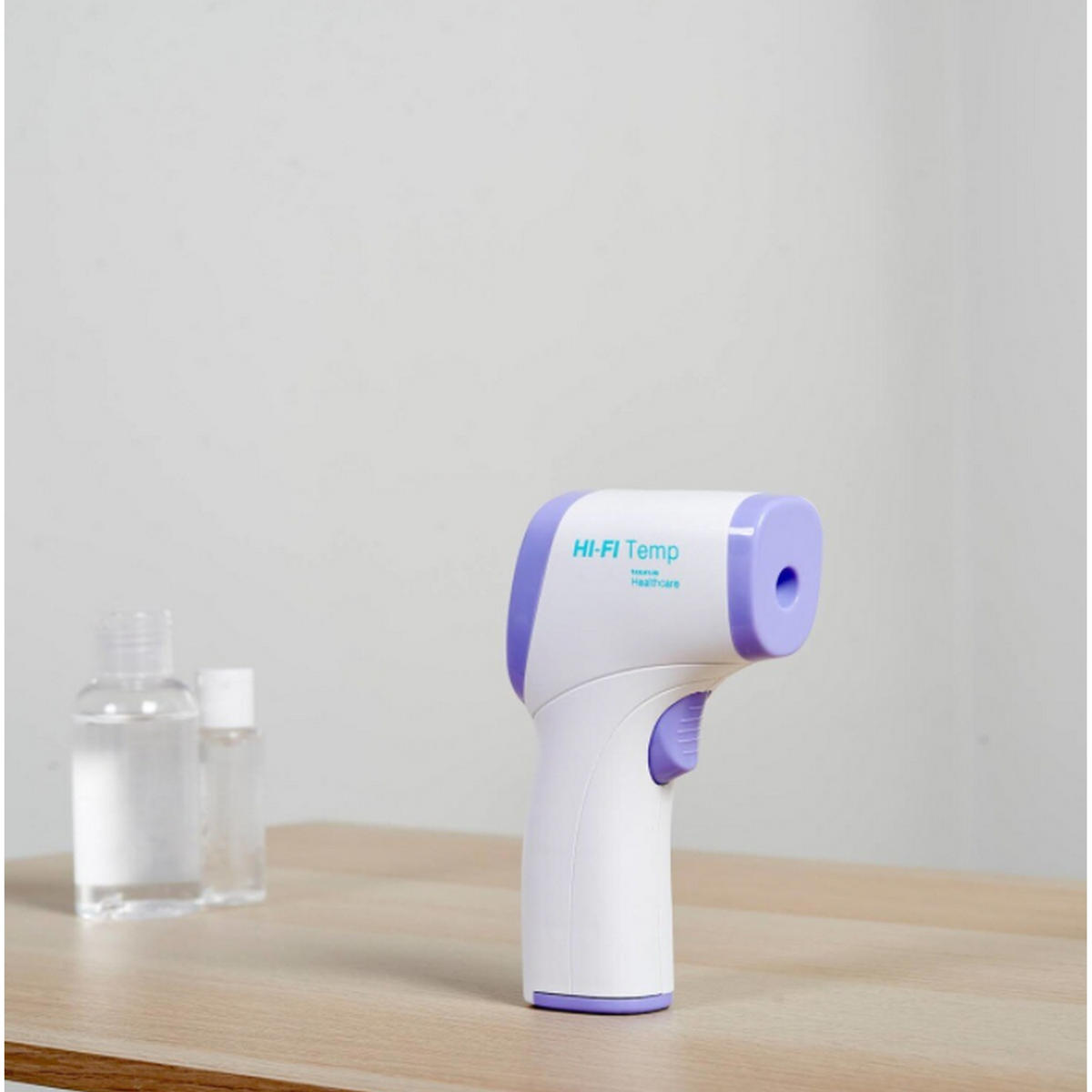 Termometro frontale bianco e viola con due bottiglie di liquido trasparente su una superficie in legno.