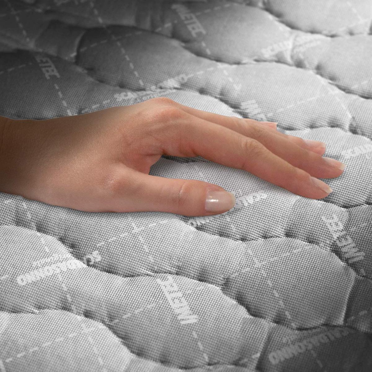 Dłoń spoczywająca na pikowanej szarej powierzchni, prawdopodobnie materacu, ujęcie z bliska.