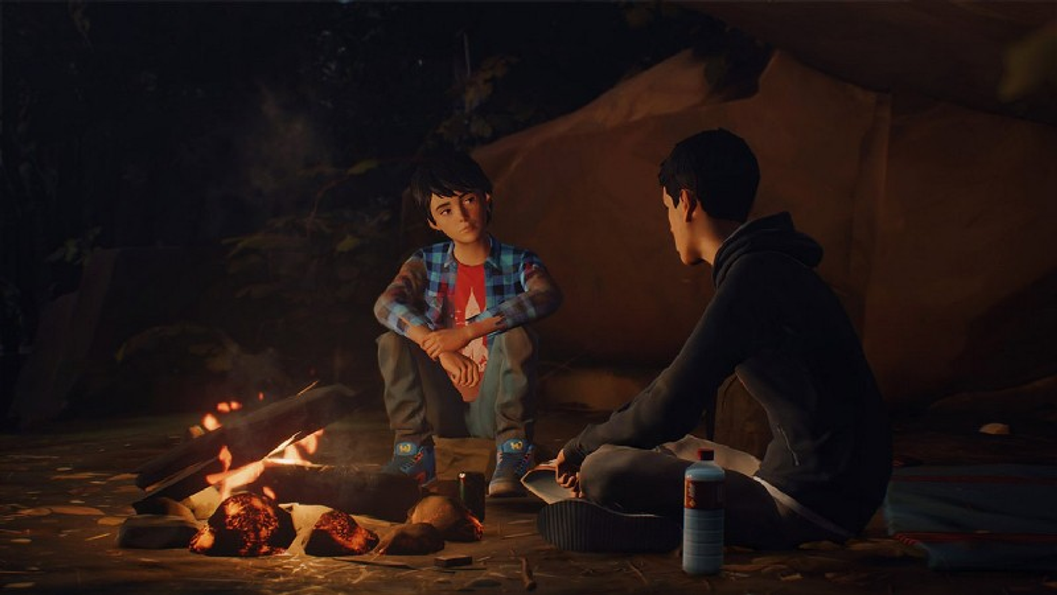 Dos chicos sentados junto a una fogata. Uno está hablando. La escena es un bosque de noche.