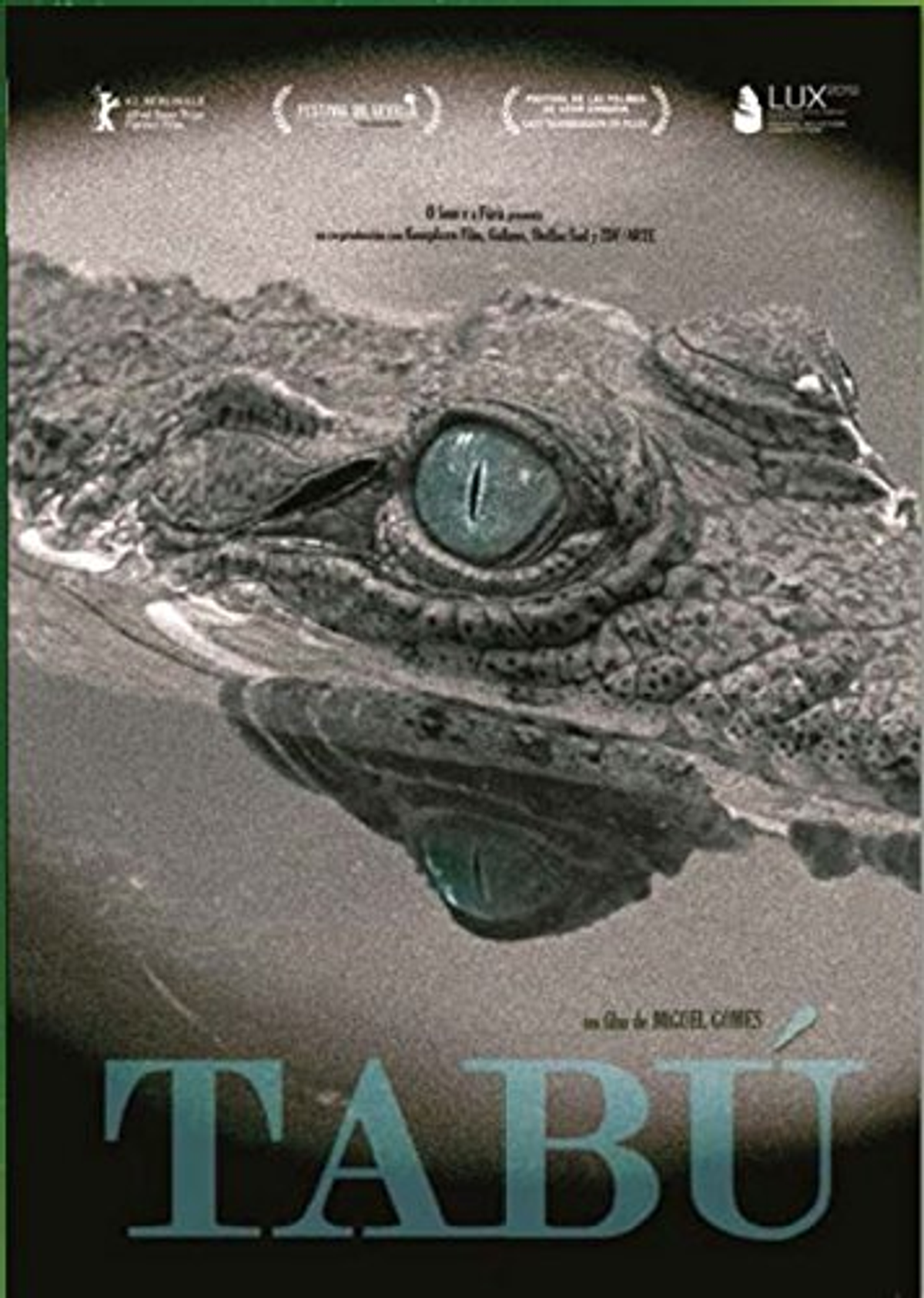 Póster muestra primer plano del ojo de un caimán, con agua. Título 'TABÚ' en la parte inferior. Fondo borroso.