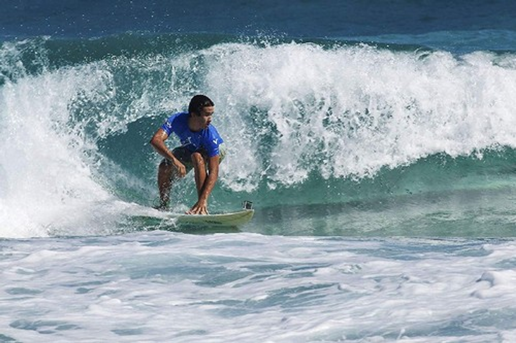 Surfista en una ola, agua azul, día brillante.