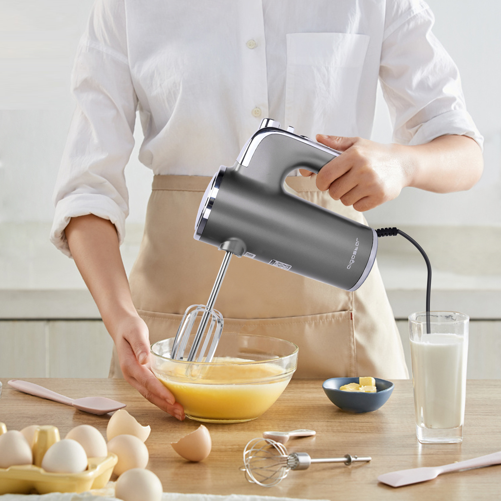 Persona usando una batidora eléctrica gris en una cocina, mezclando huevos en un tazón.