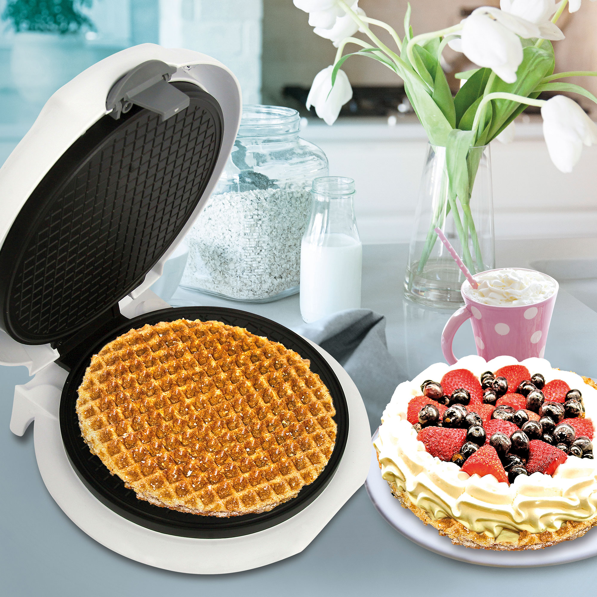 Waffle iron with a cooked waffle, and a cake with berries and whipped cream.