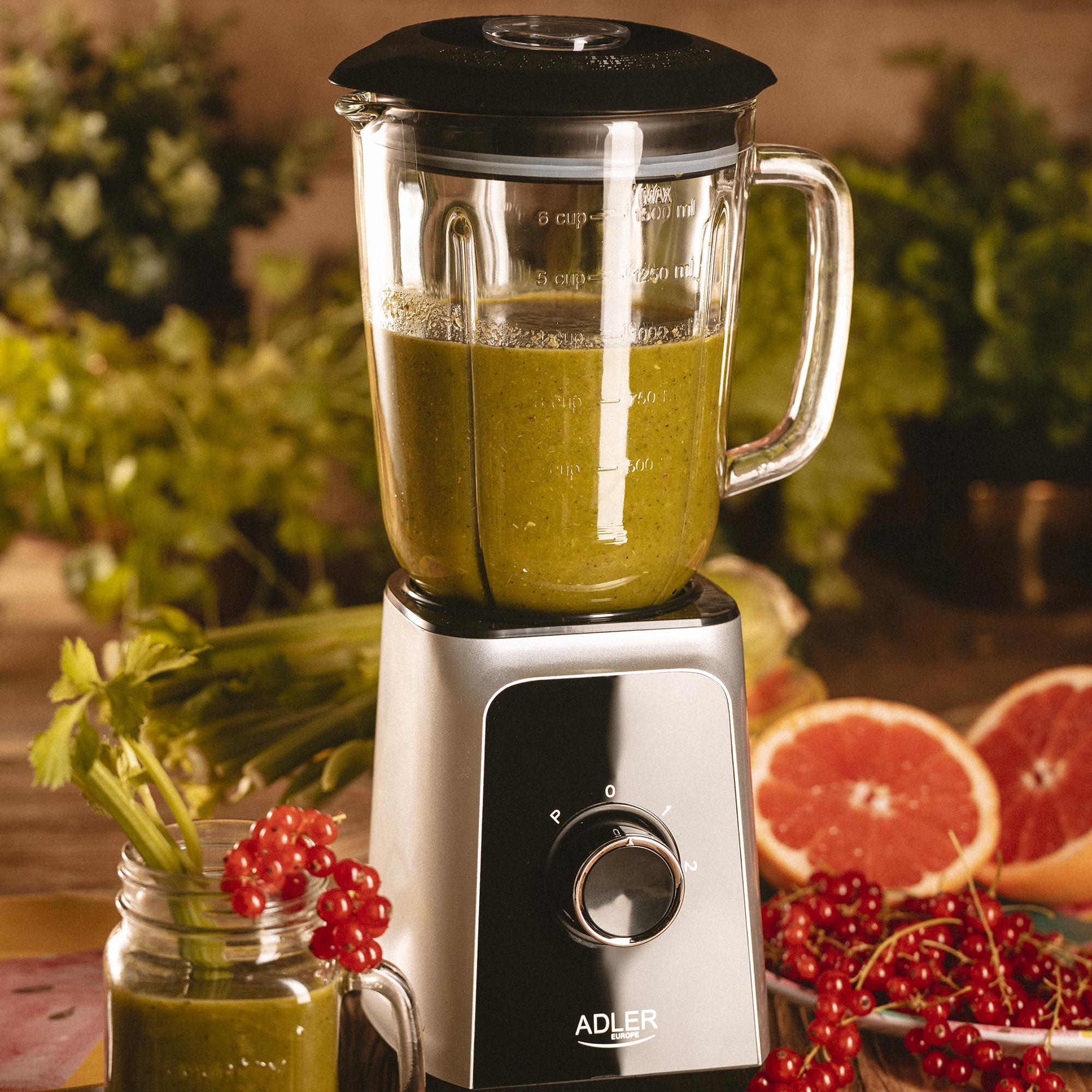 Blender z zielonym koktajlem, z szklanką koktajlu i owocami z boku.