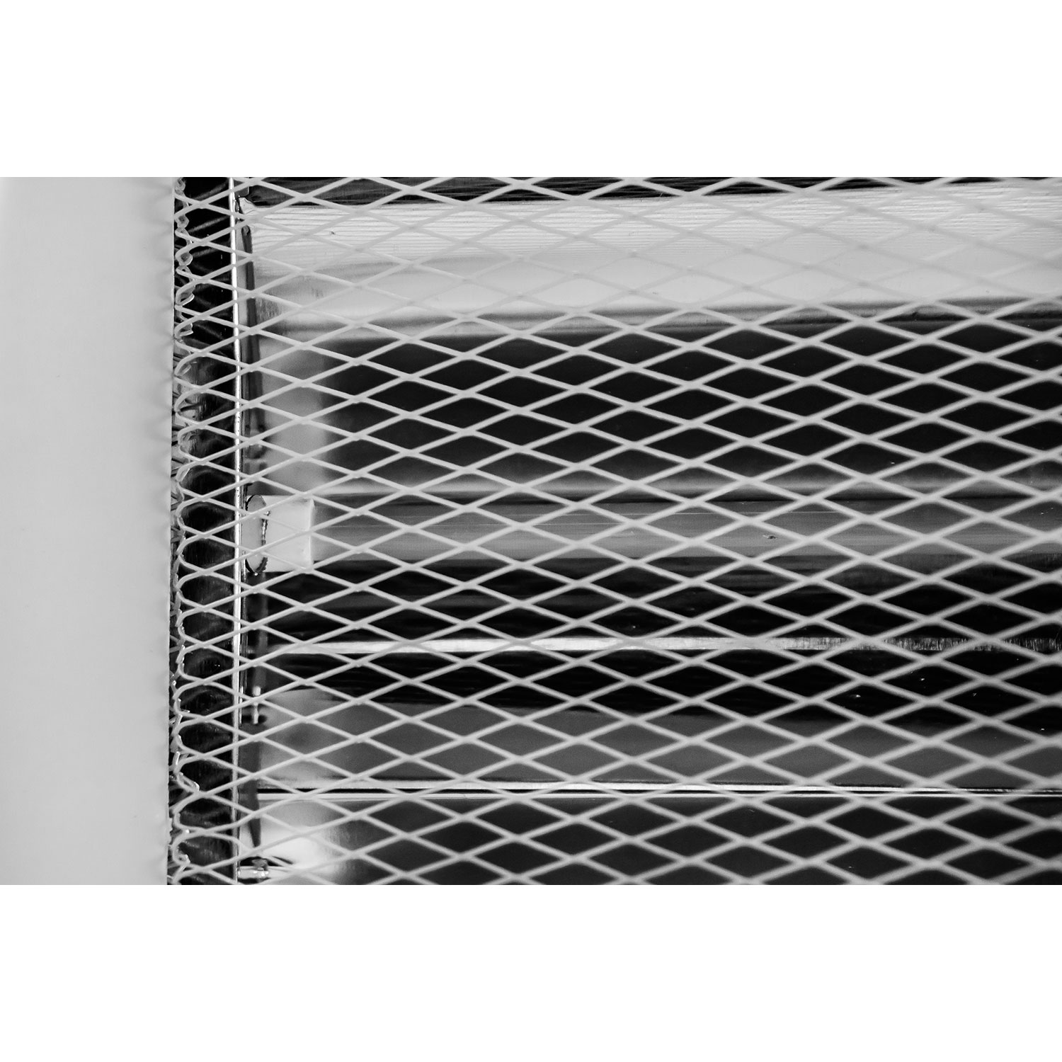 Primer plano de una rejilla metálica, probablemente una rejilla de ventilación, con borde blanco sobre una superficie blanca.