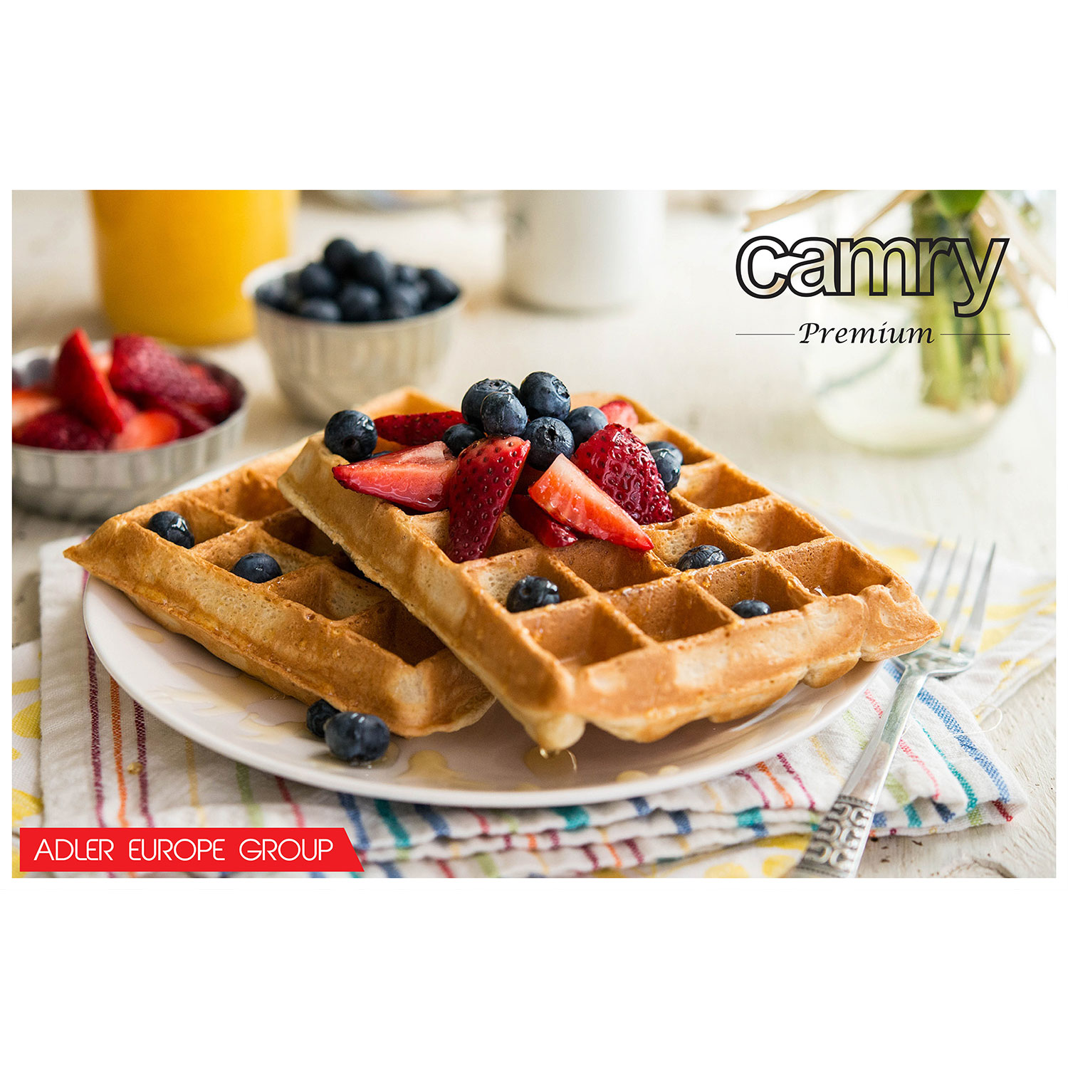 Zwei Waffeln mit Erdbeeren und Blaubeeren auf einem Teller. Saft und Beeren in Schalen sind im Hintergrund.