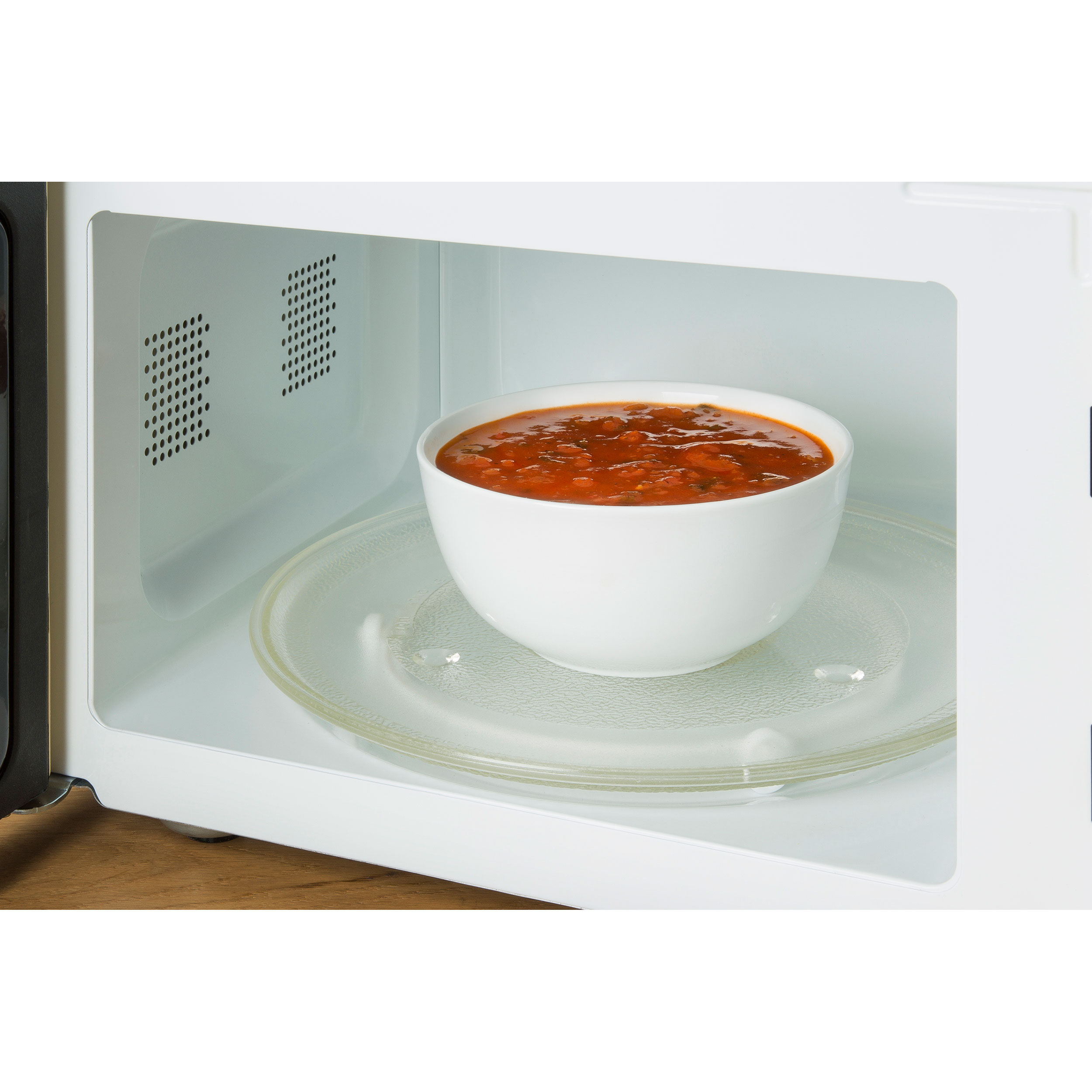 Mikrowelleninnenraum mit einer Schüssel Tomatensuppe auf einem Glasteller. Hintergrund weiß.