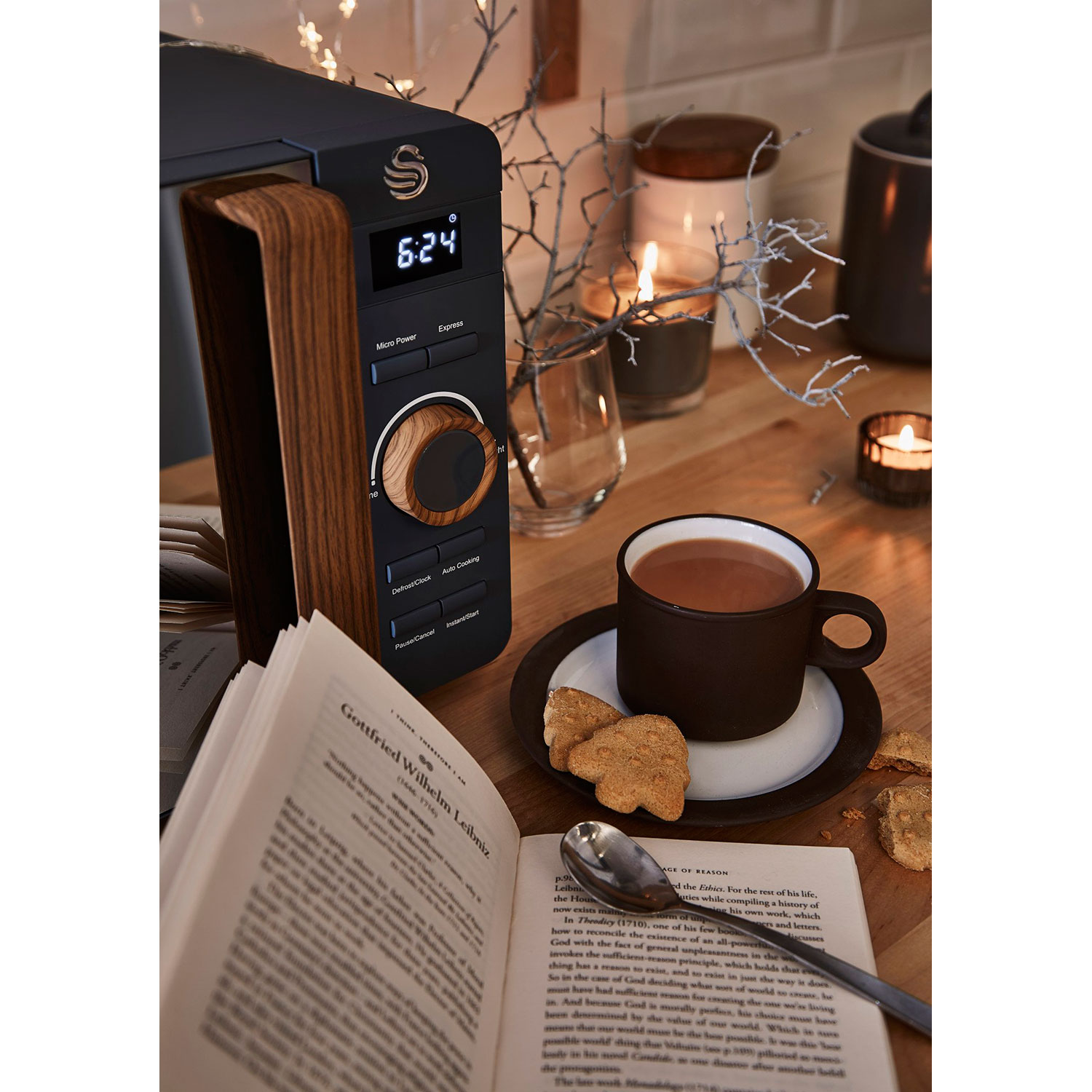 Mikrowelle mit Holzgriff neben einem Tisch mit Buch, Becher und Kerzen.