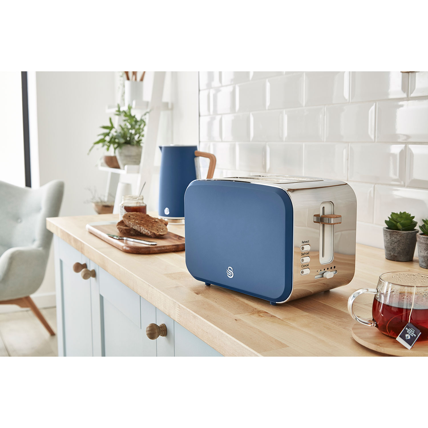 Blauer und silberner Toaster auf einer Arbeitsplatte mit Brot und Tee.