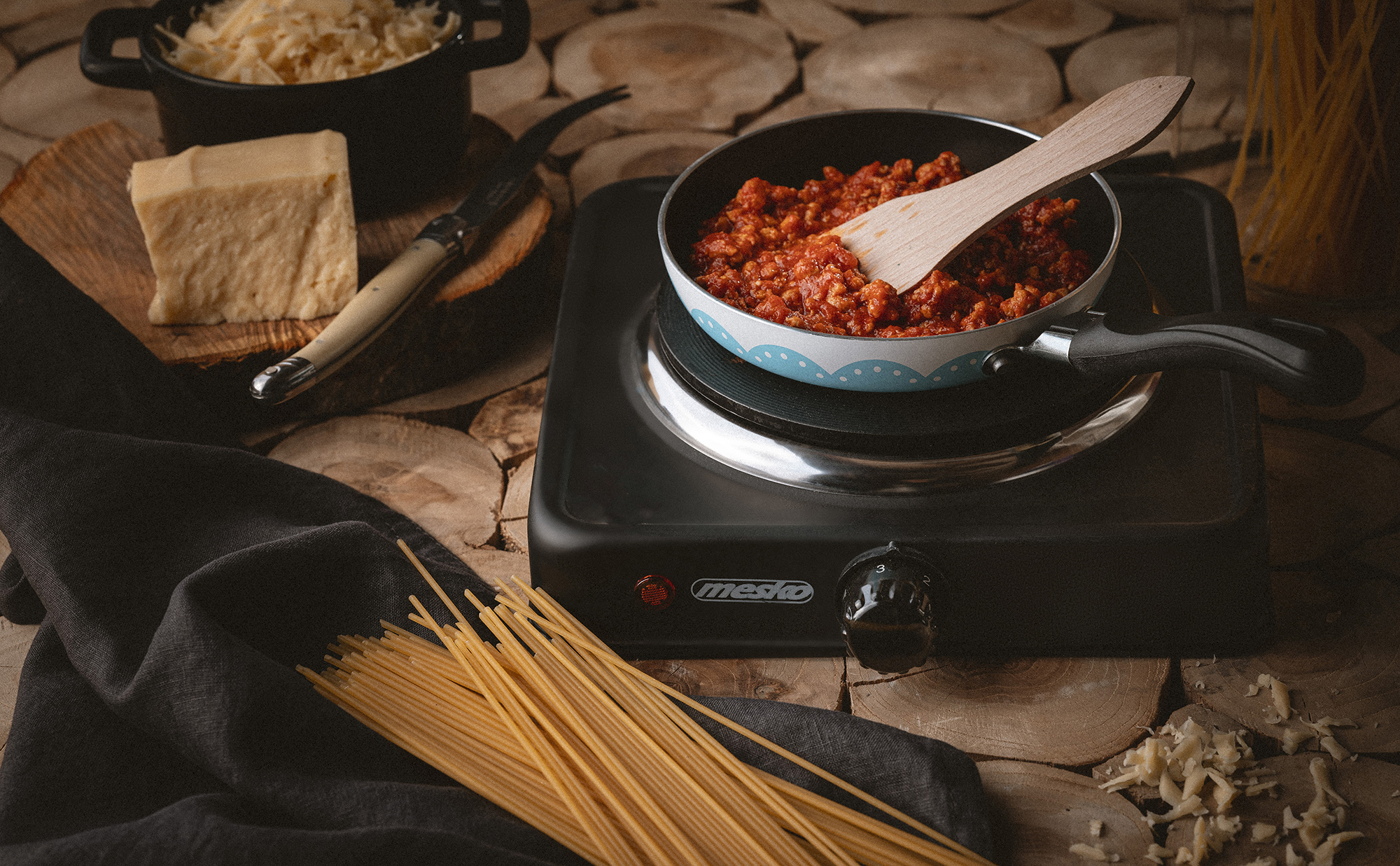 Patelnia z sosem do makaronu i drewnianą łyżką na czarnej płycie kuchennej ze składnikami.