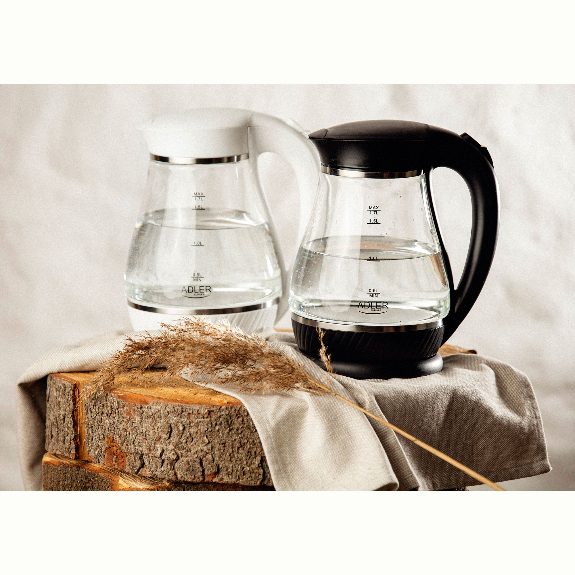 Dwa szklane czajniki z wodą w środku. Jeden jest biały, a drugi czarny. Umieszczone na drewnie i tkaninie.