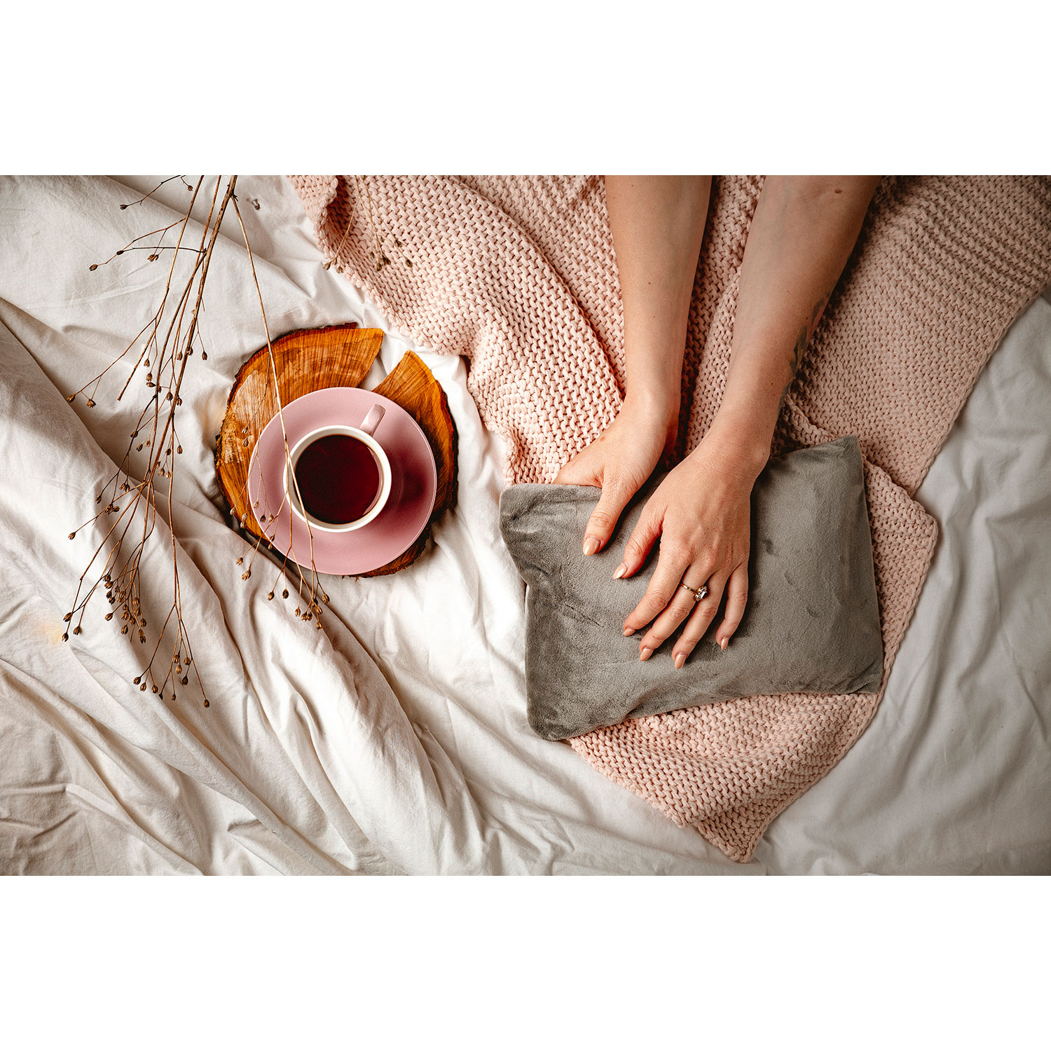 Una taza de té en un platillo rosa y una almohada gris en una cama con una manta rosa.