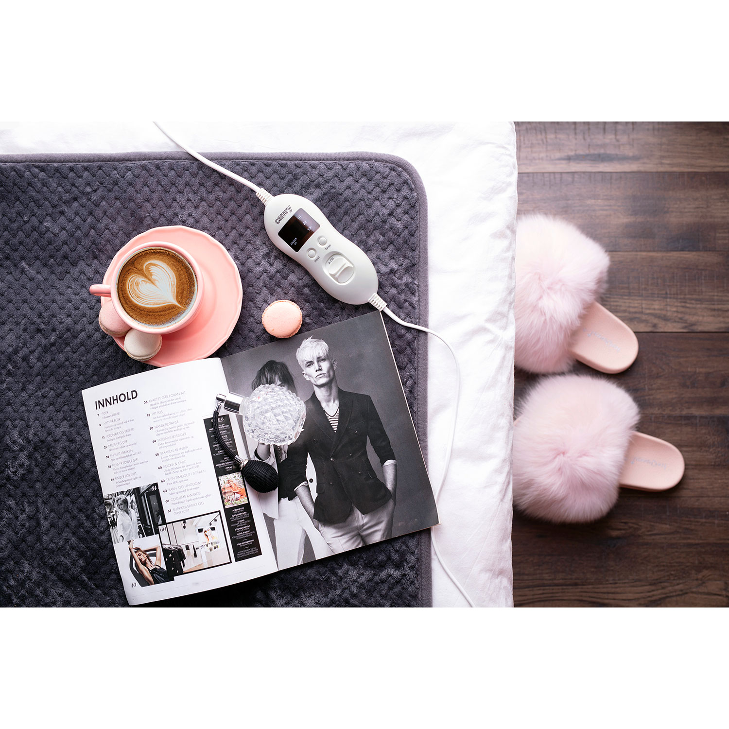Configurazione letto con scaldaletto, caffè, libro e pantofole rosa.