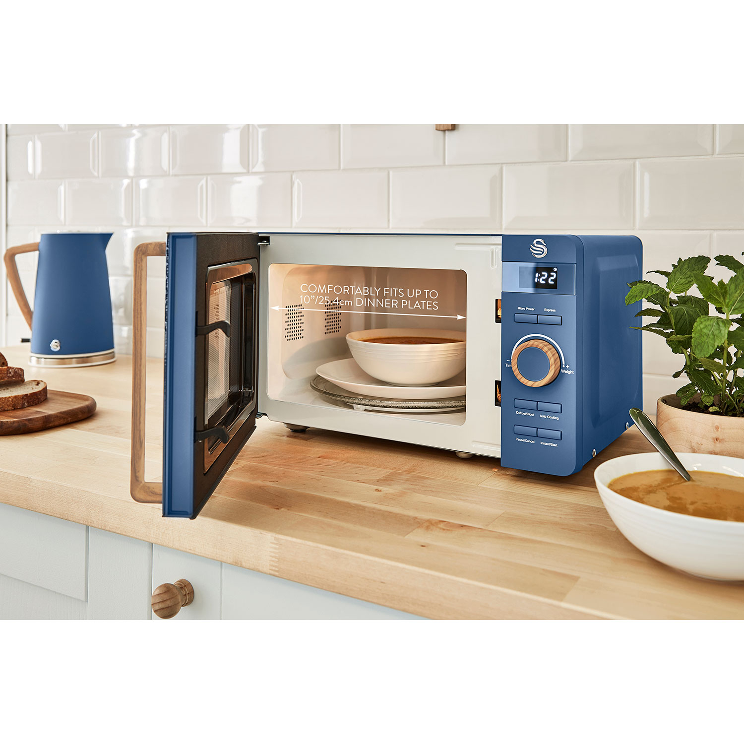 Horno microondas azul con puerta abierta, tazón de sopa dentro, en mostrador madera.