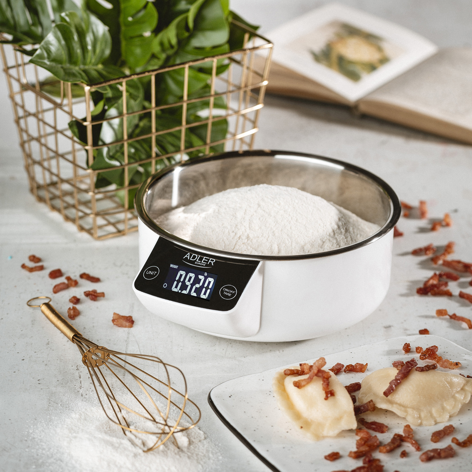 Waga z mąką, trzepaczką, jedzeniem i rośliną w koszu na stole.