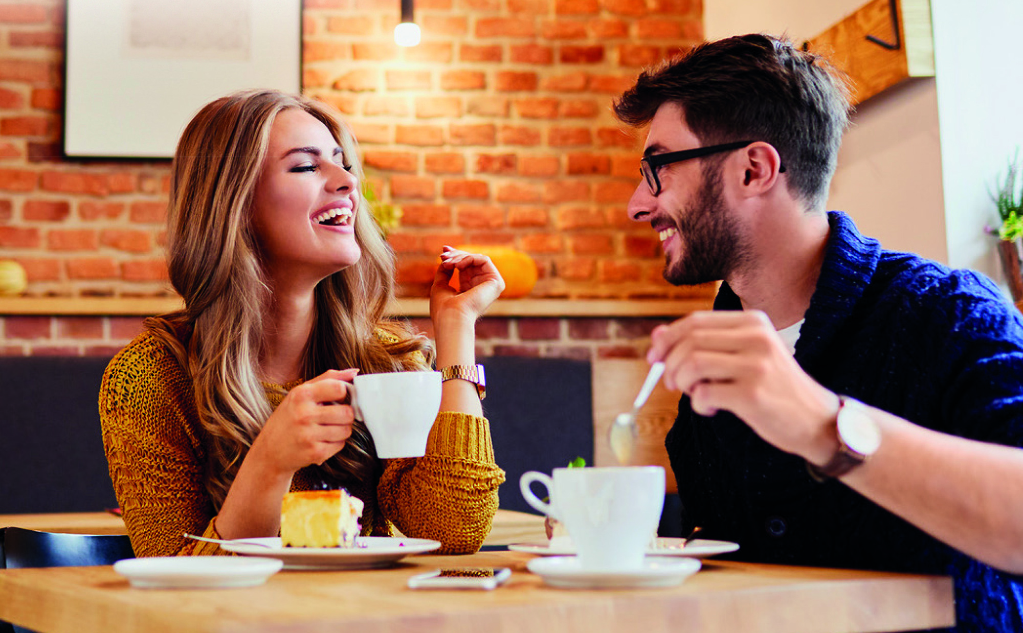 Ein Paar lacht über Kaffee in einem Café. Ein Stück Kuchen liegt auf dem Tisch.