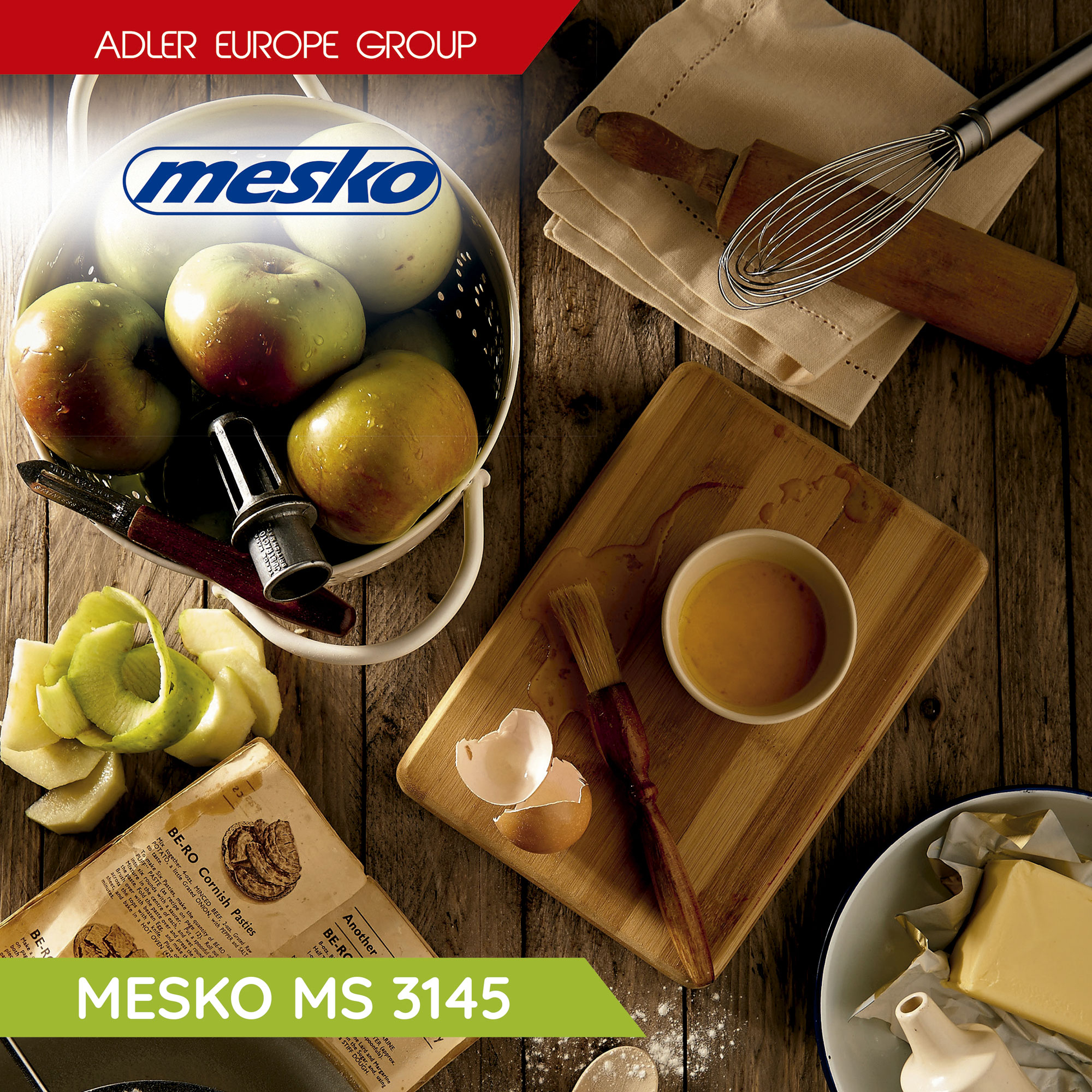 Drewniany stół ze składnikami do gotowania: jabłka, jajka, masło, wałek, trzepaczka i deska do krojenia. Widoczne logo Mesko.