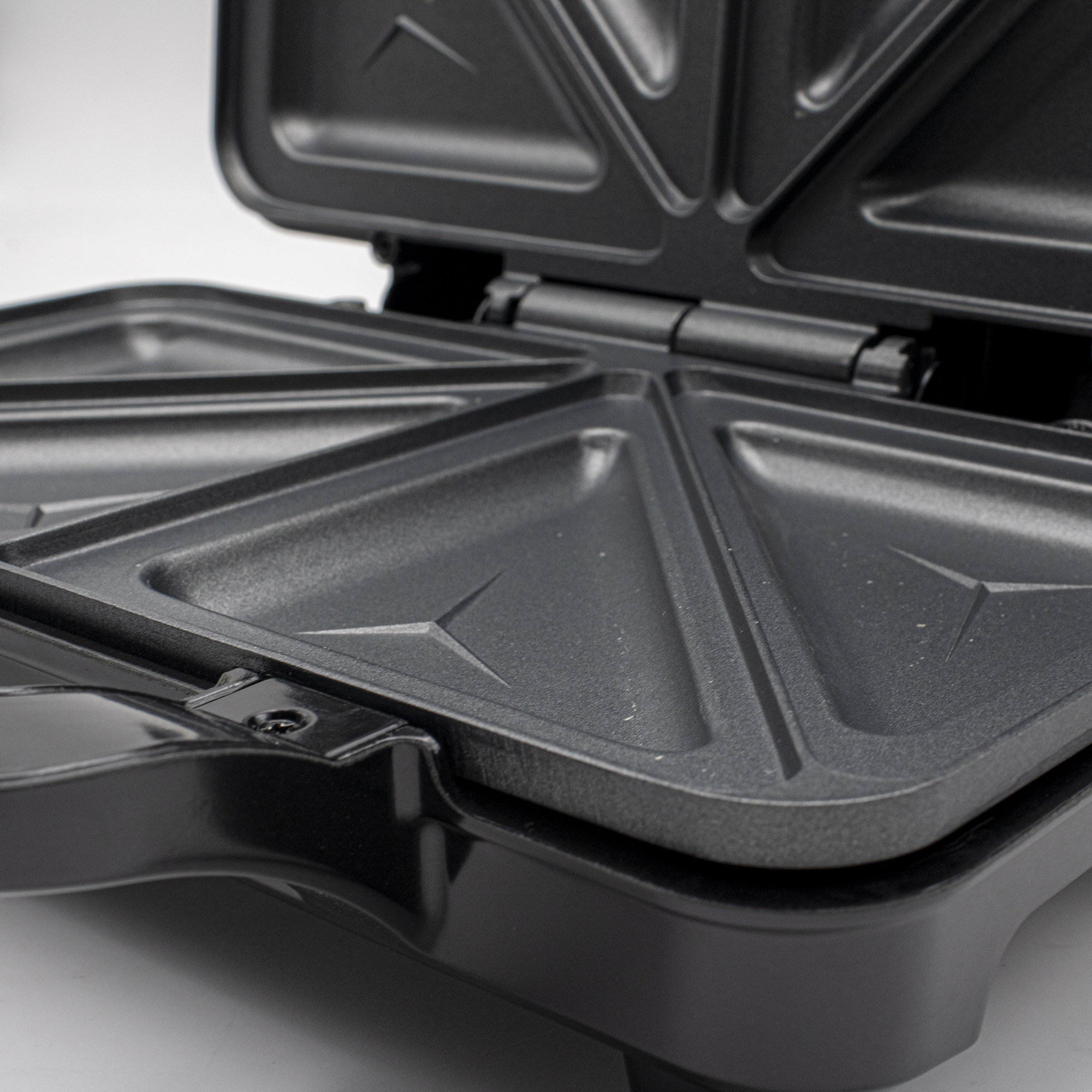 Zbliżenie czarnego opiekacza do kanapek z trójkątnymi płytami.