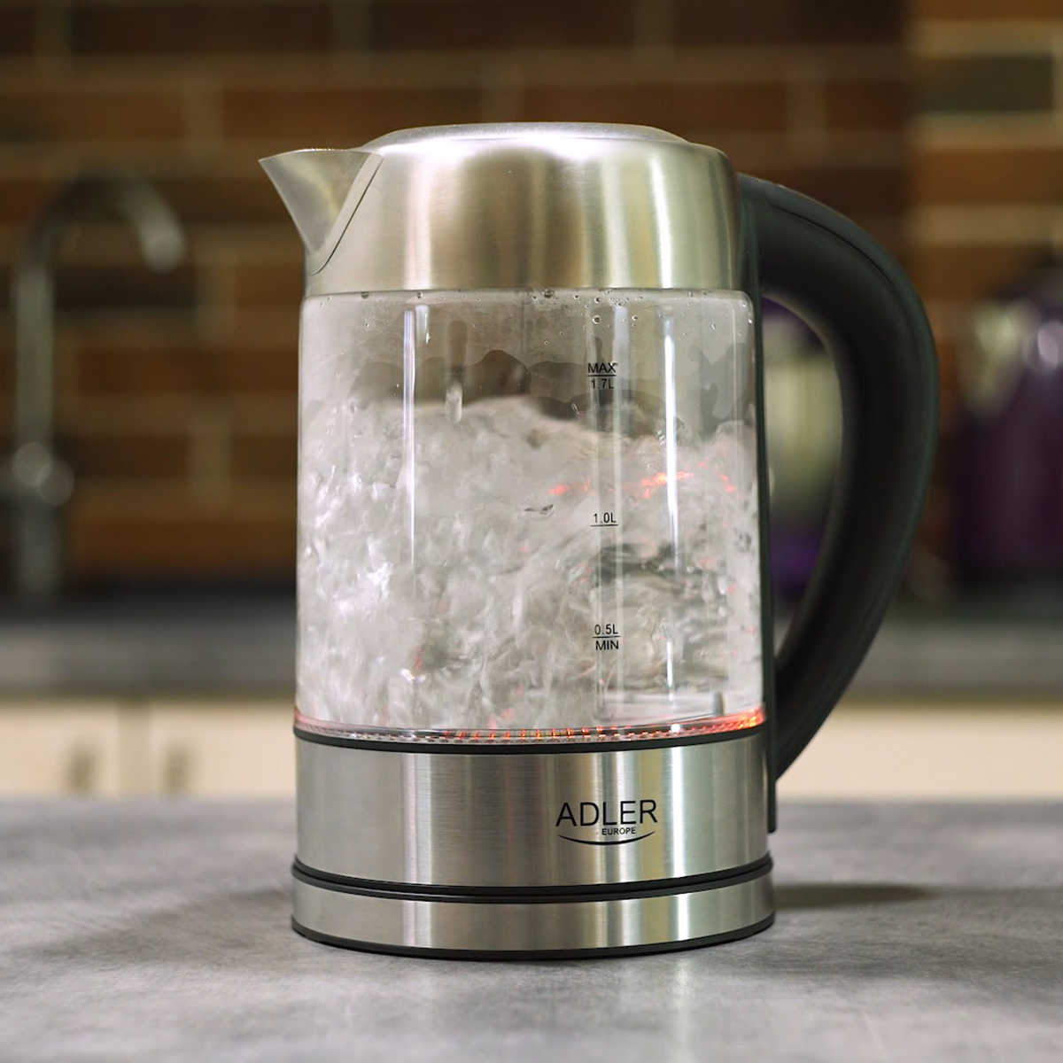 Srebrny i szklany czajnik elektryczny z wrzącą wodą w środku.