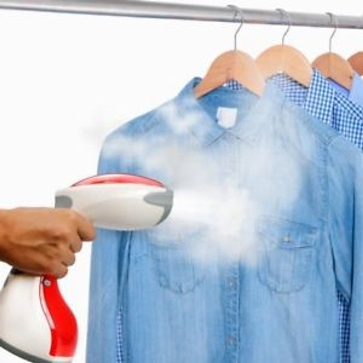 Una plancha de vapor está planchando una camisa azul colgando en un perchero.