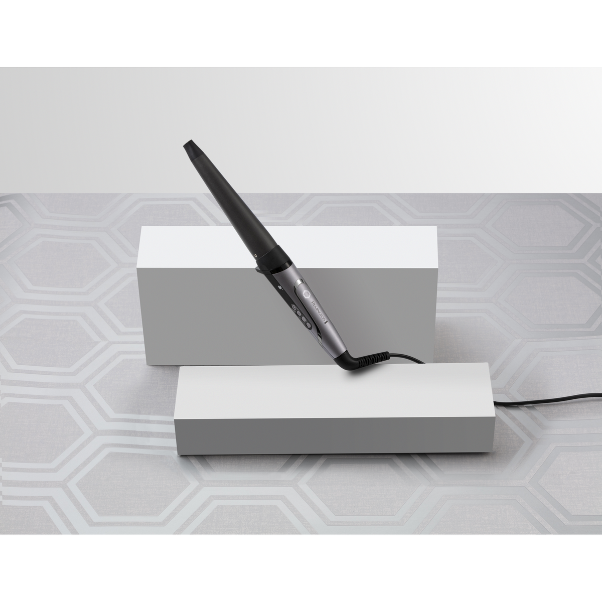 Czarna i srebrna lokówka Remington na białych podestach, z czarnym kablem.