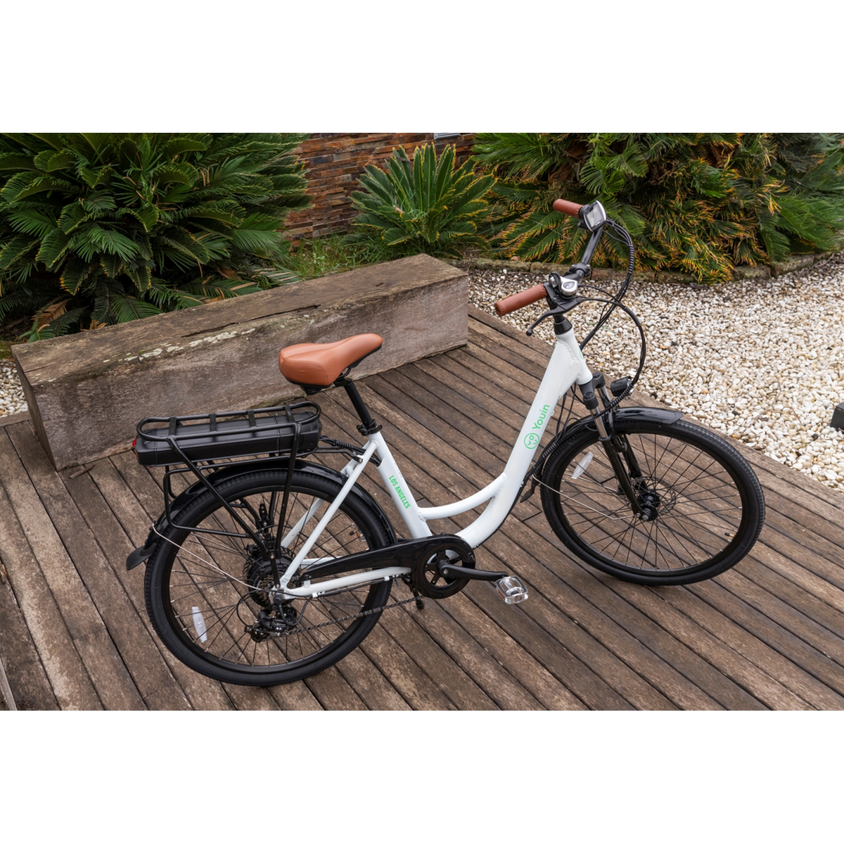 Bicicleta eléctrica blanca en una plataforma de madera rodeada de vegetación, con asiento marrón.