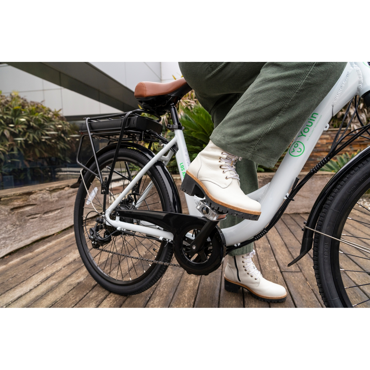 Persona montando bicicleta blanca y negra con asiento marrón, usando botas blancas.