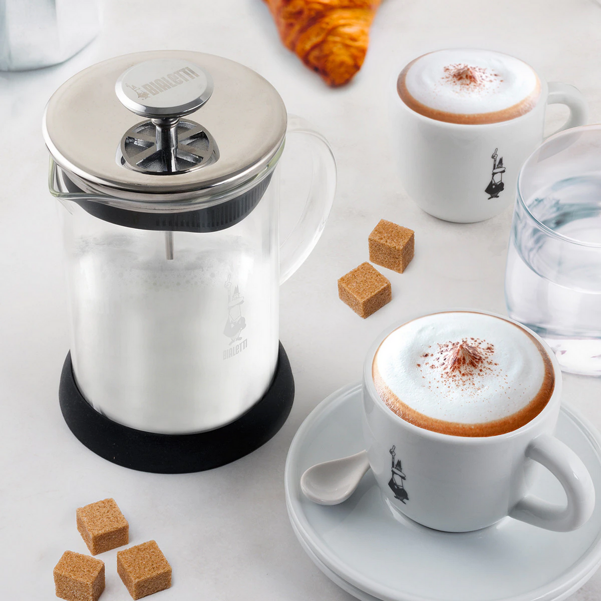 Dzbanek do kawy z dwiema filiżankami cappuccino i kostkami cukru na stole.