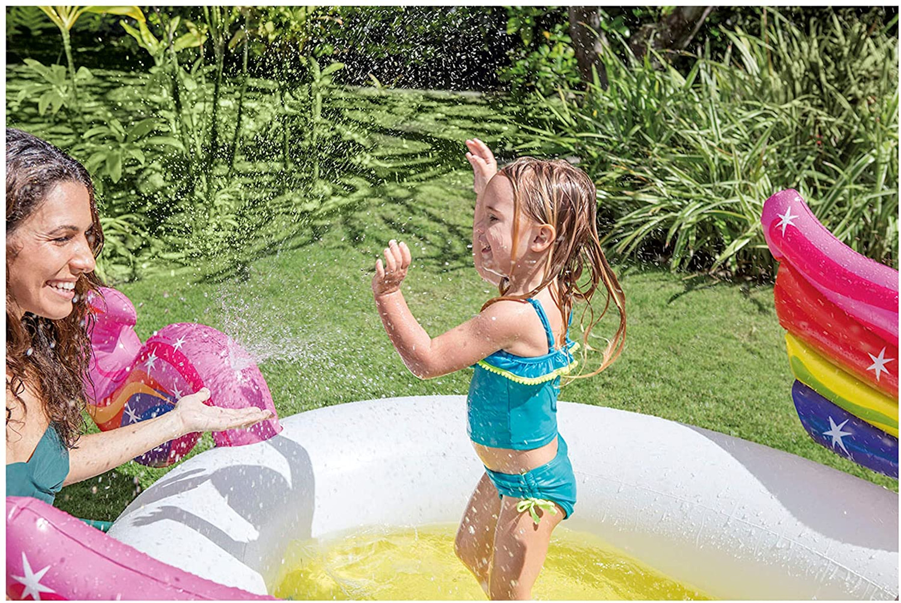 Frau und Kind spielen in einem Pool mit Einhorn-Schwimmreifen, spritzen Wasser.