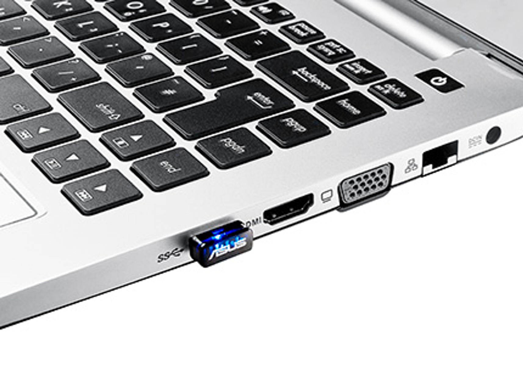 Teclado de portátil con un dongle USB ASUS conectado. Puertos HDMI y VGA visibles lateralmente.