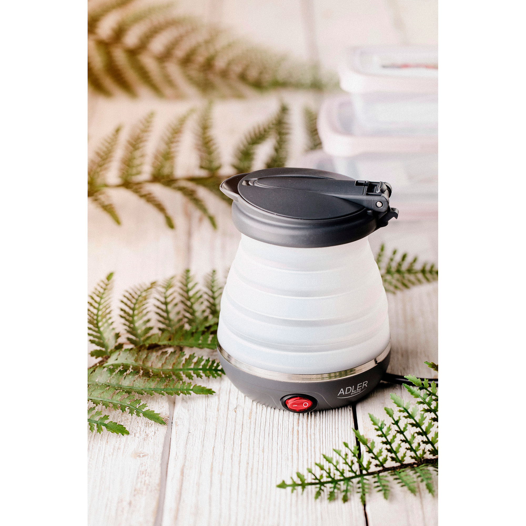 Biały i czarny składany czajnik na drewnianej powierzchni z paprociami i plastikowym pojemnikiem.